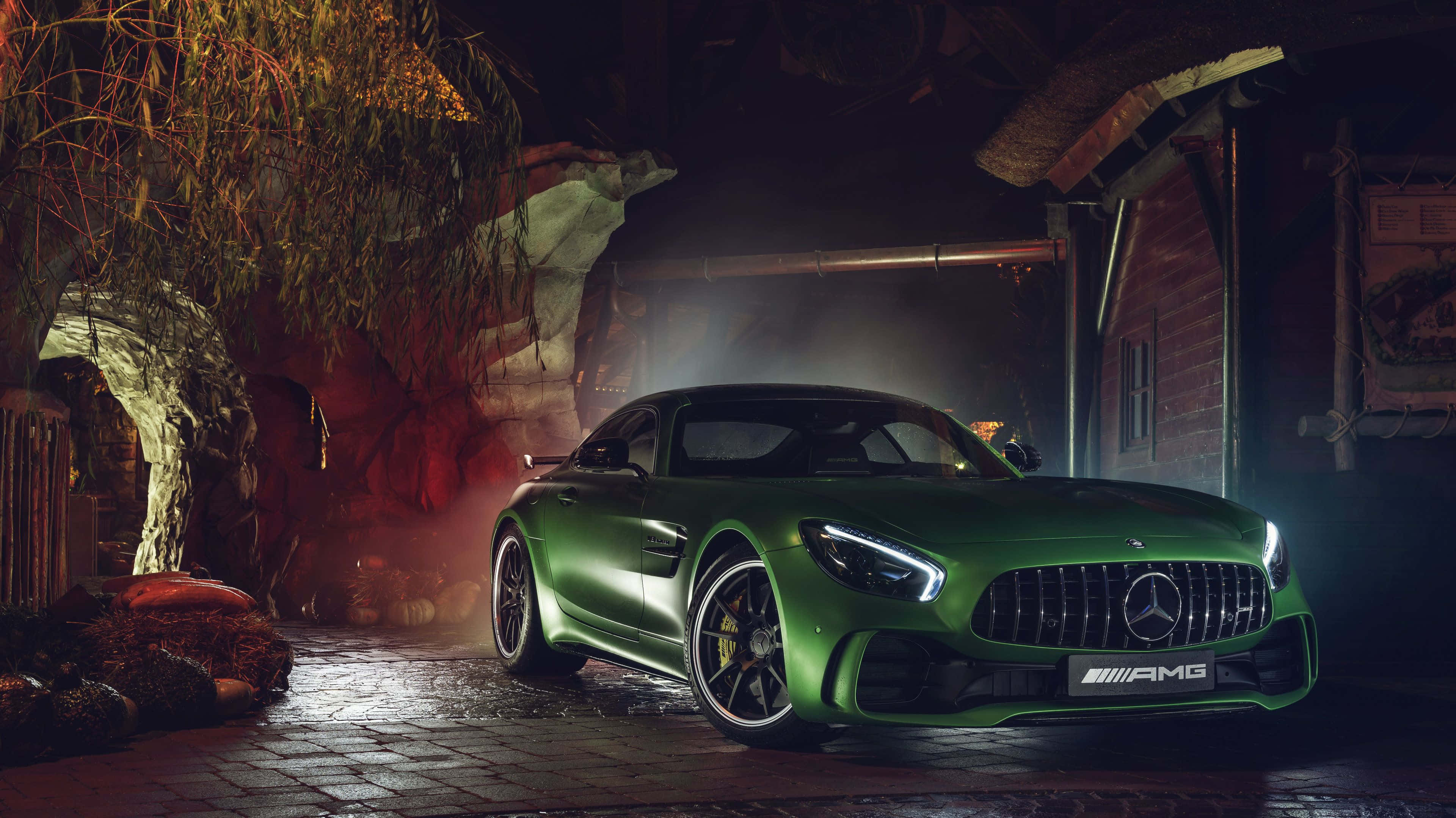 停泊於夜街的綠色梅賽德斯-AMG GT R 壁紙 — 一輛光澤的綠色Mercedes-AMG GT在夜間停放在一個霧氣瀰漫、質樸的石頭車庫中，帶有戲劇性的燈光。
