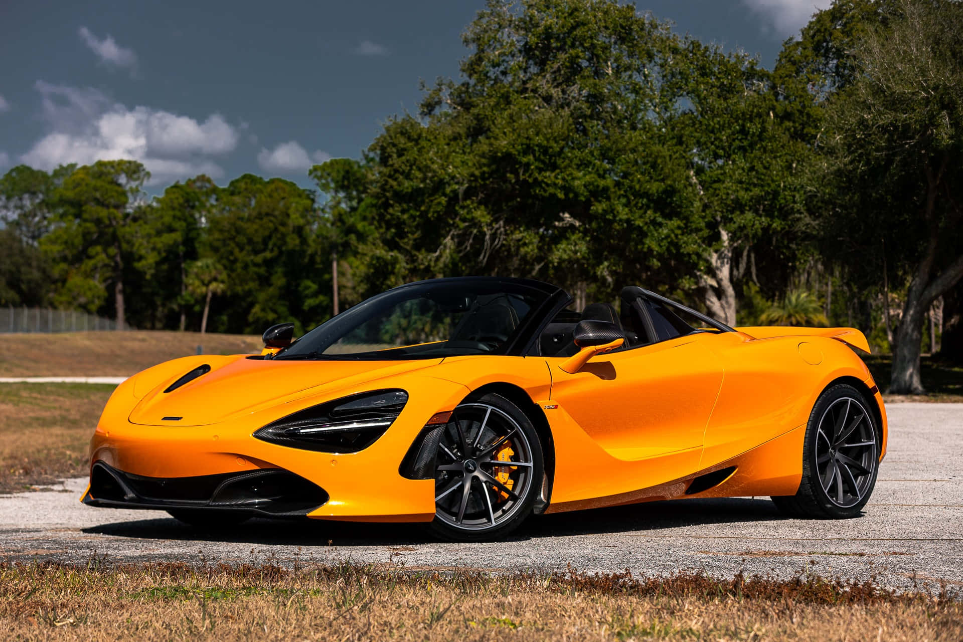 橙色McLaren 720S Spider開篷車停在戶外樹木附近。