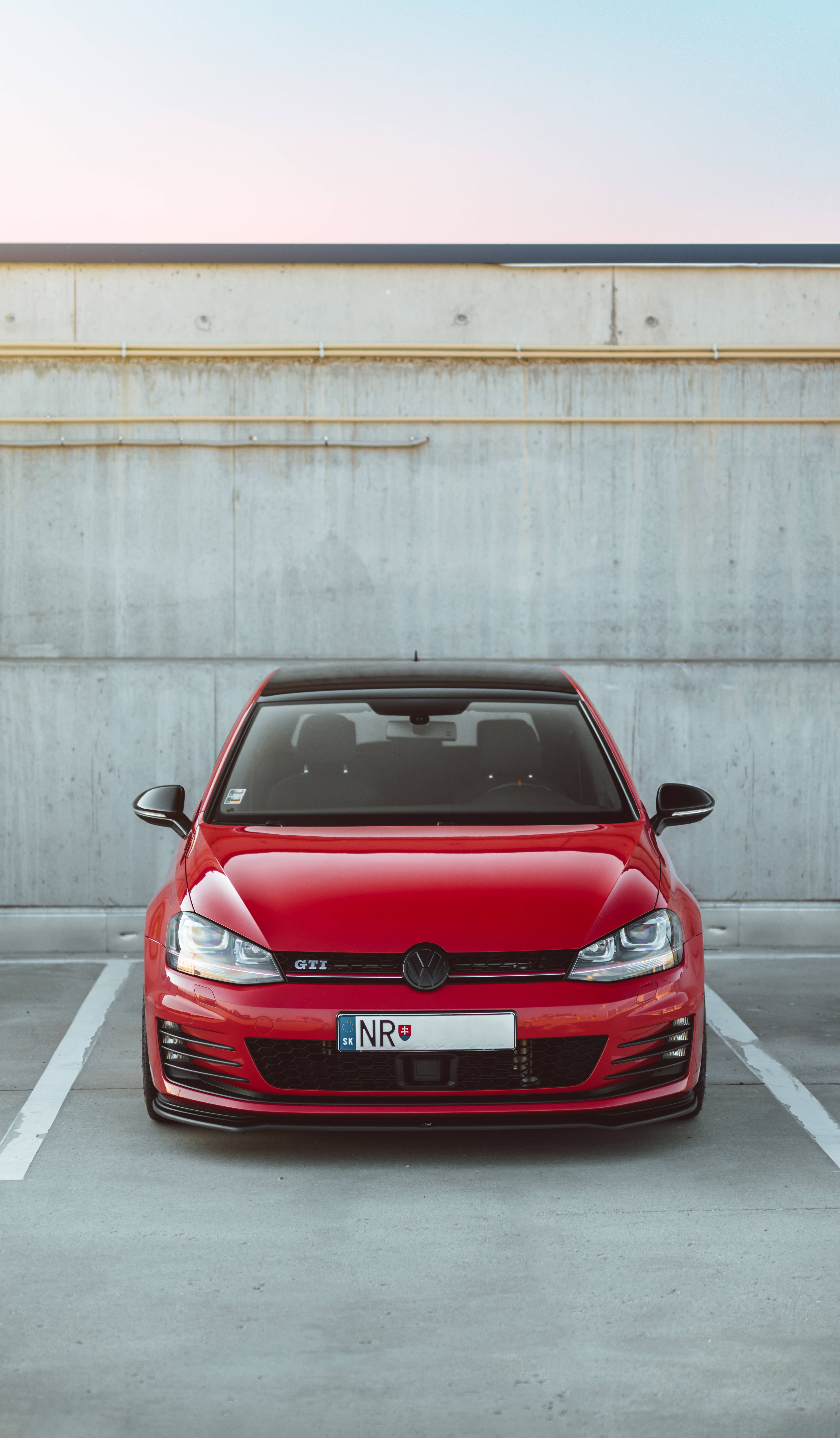 停泊的紅色VW Golf GTI 壁紙 — 一輛鮮紅色的福士Golf GTI停在混凝土停車場，背景是柔和粉紅與藍色的暮色天空。