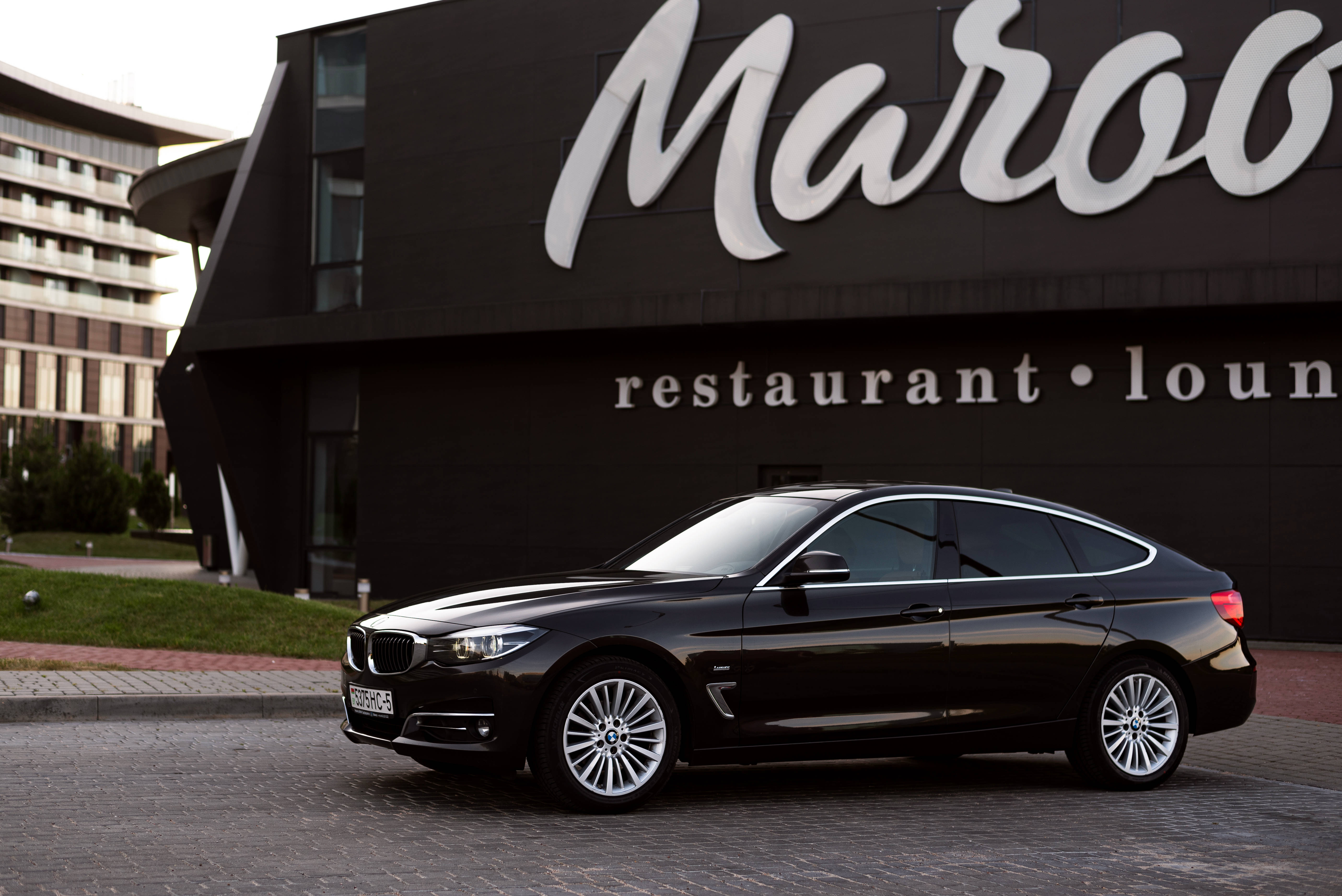 停泊的黑色寶馬 壁紙 — 一輛時尚的黑色BMW Gran Coupe停在現代黑色建築前的鵝卵石車道上，建築物上有「Maroo restaurant lounge」標誌。