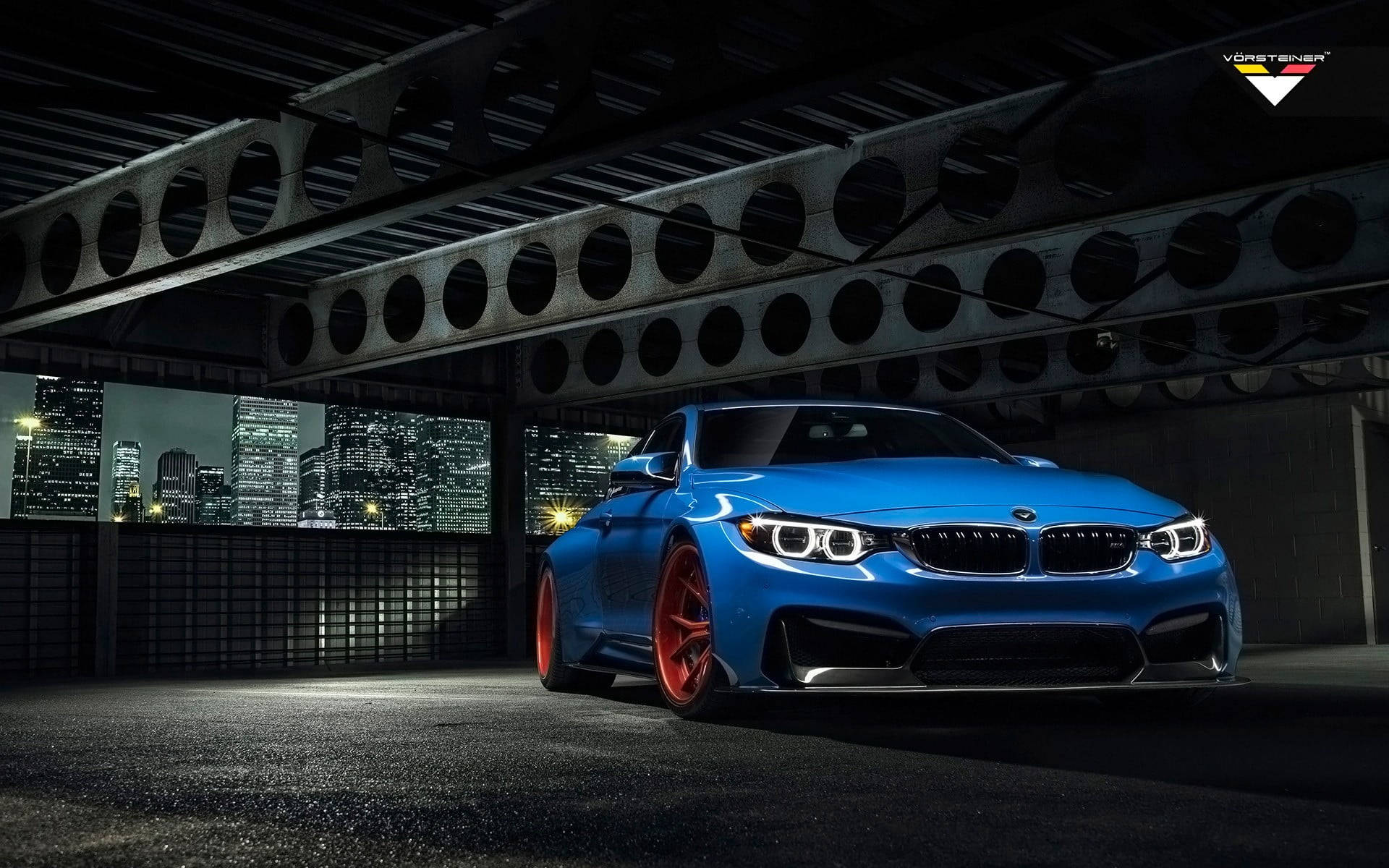 藍色BMW M4配紅色輪圈，夜間停在橋下，背後是城市燈光。
