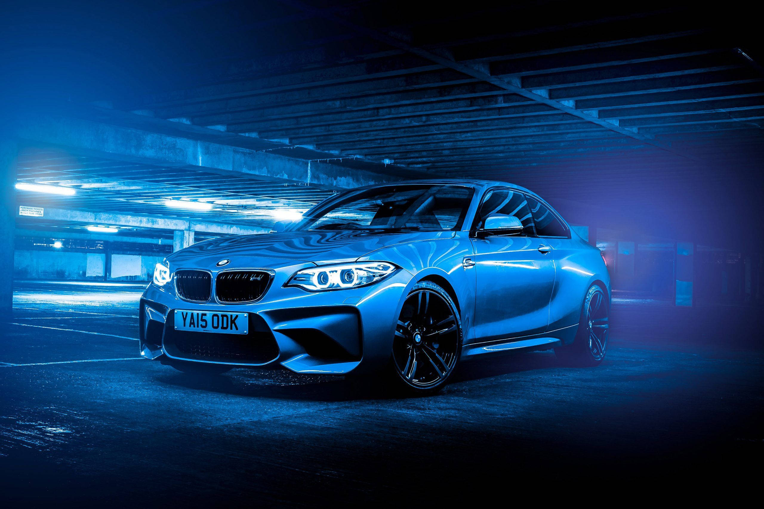 停車場內發光的藍色BMW 壁紙 — 一架時尚的藍色BMW M2雙門轎跑車在昏暗的地下停車場中，在霓虹燈下閃閃發光。
