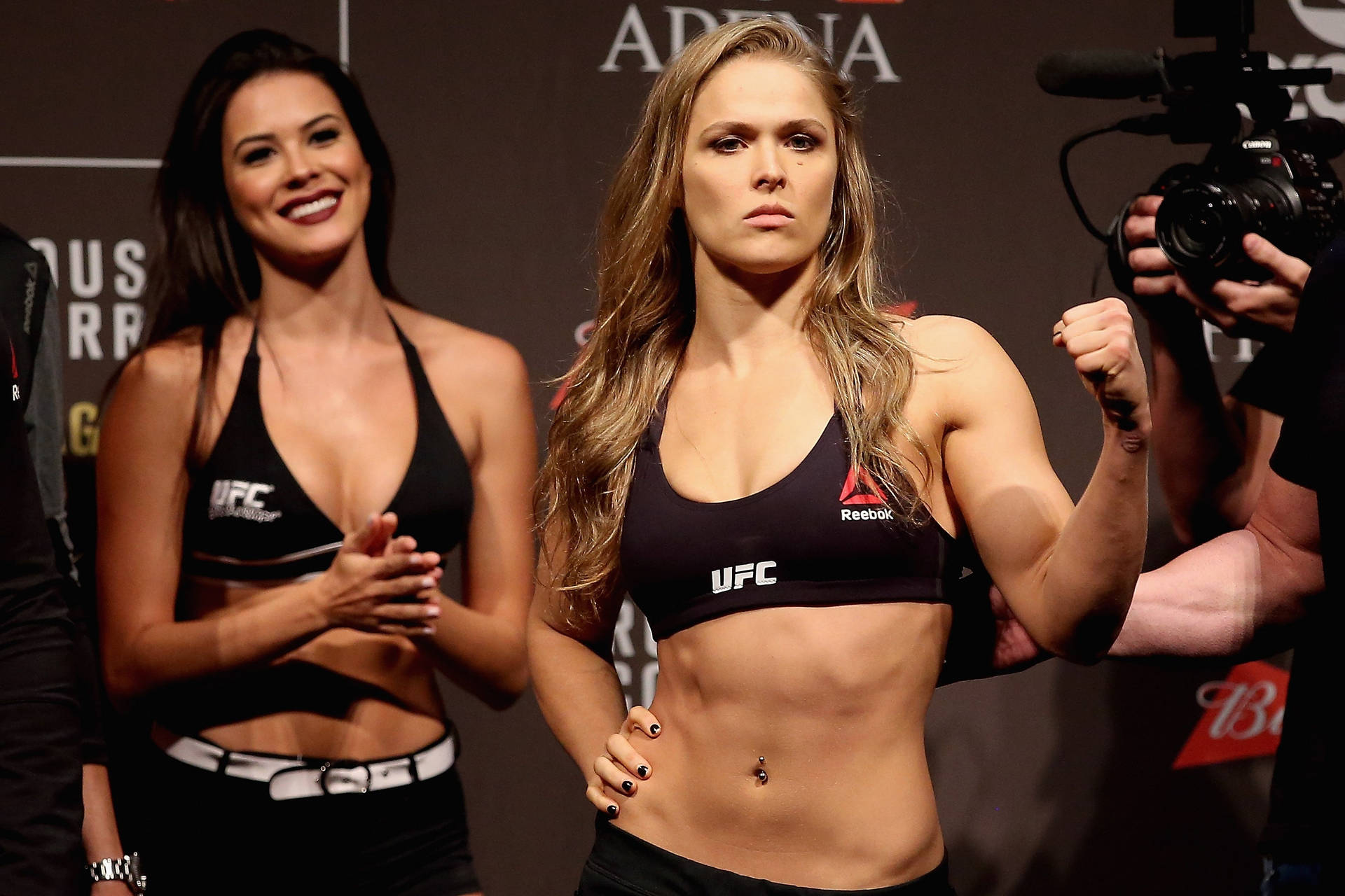 UFC拳手在稱重活動中自信地擺姿勢，旁邊有一位微笑的女性。