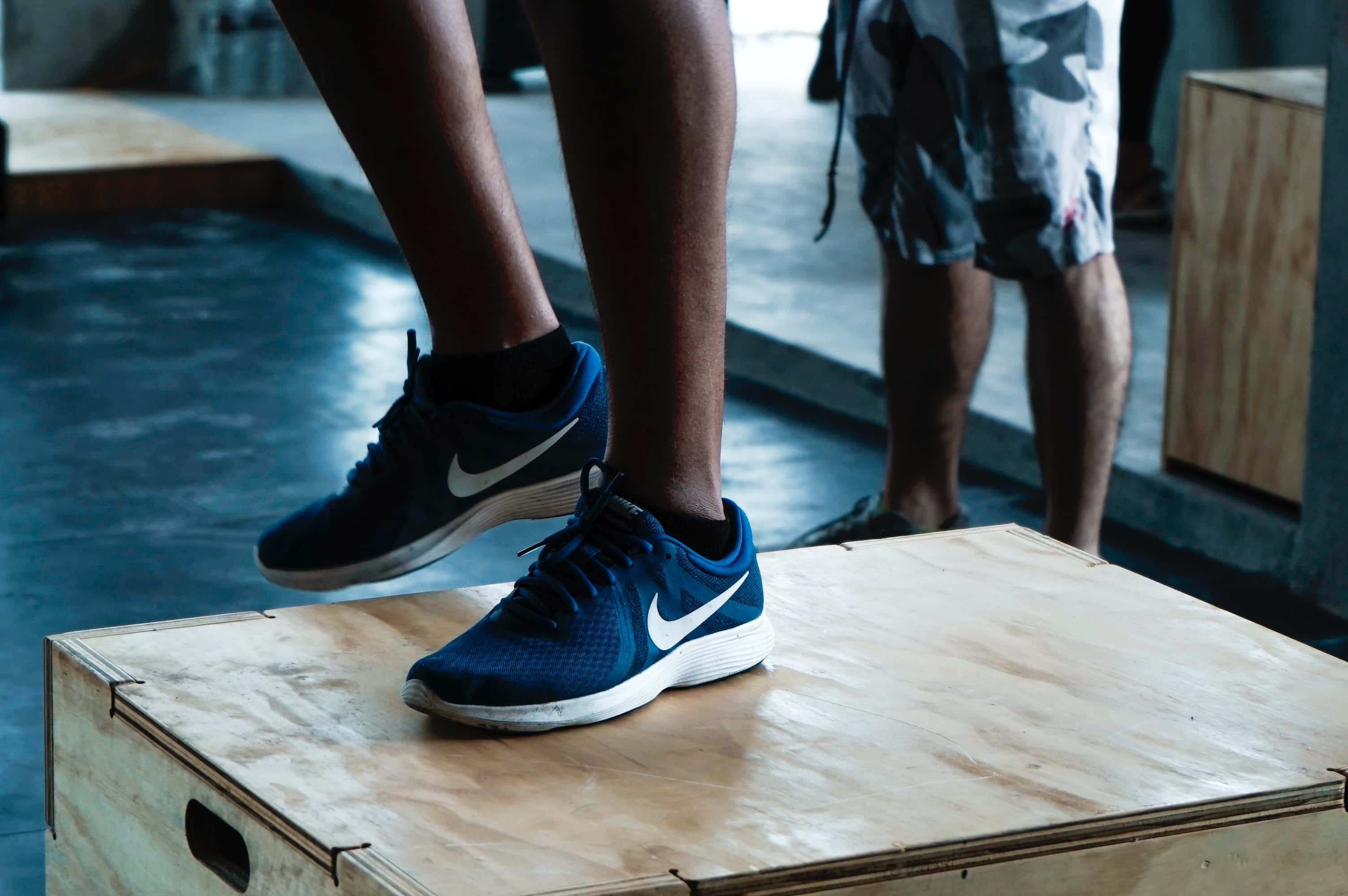 Navy Blue Shoes 桌布 壁紙 — 健身室中，藍色Nike運動鞋在木製跳箱上方半空中的特寫，背景模糊。