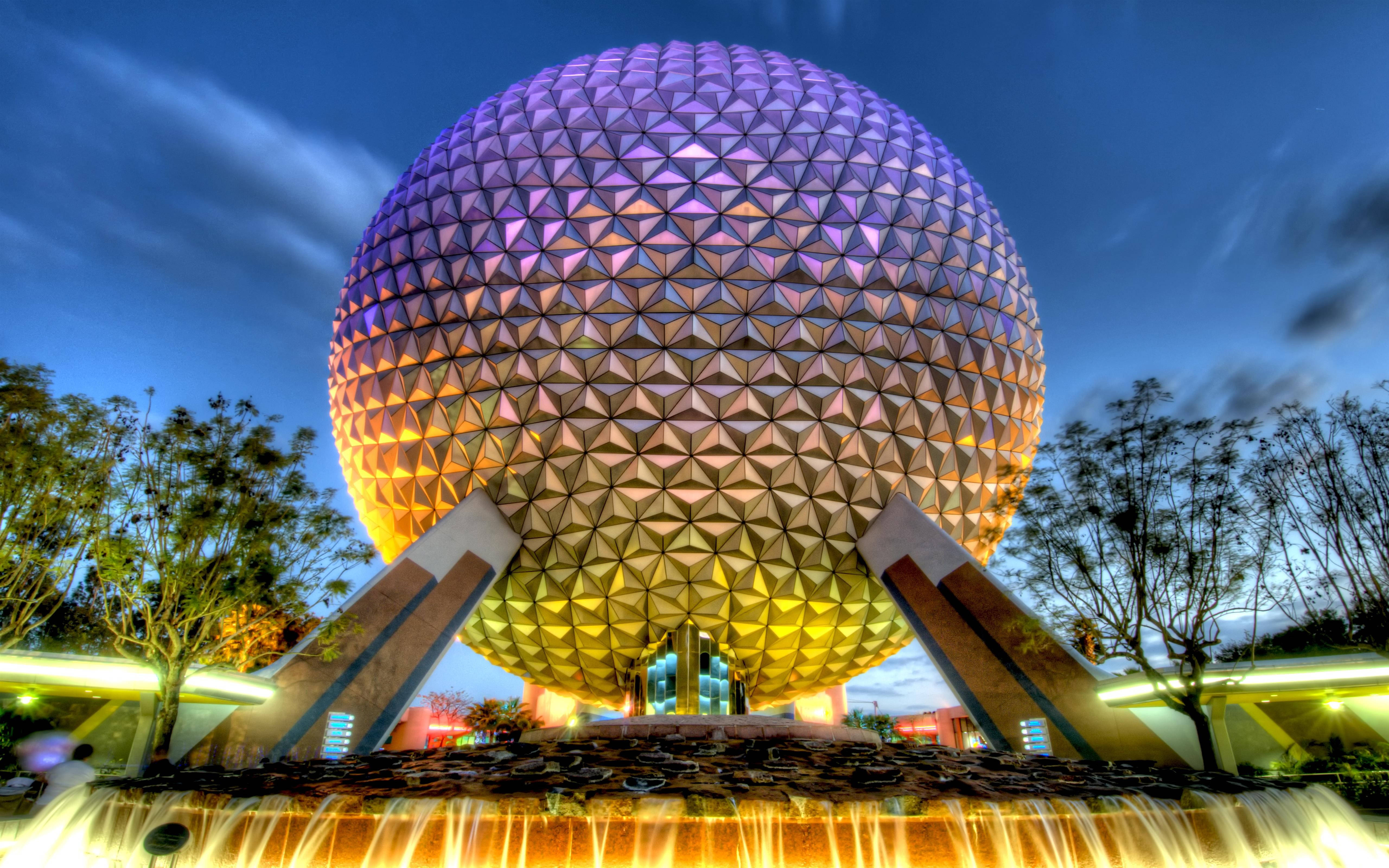 傍晚時分色彩繽紛的 Epcot 球體 壁紙 — 一個巨大的測地線球體在暮色天空下，在層疊的噴泉上方發出紫色和金色的光芒。