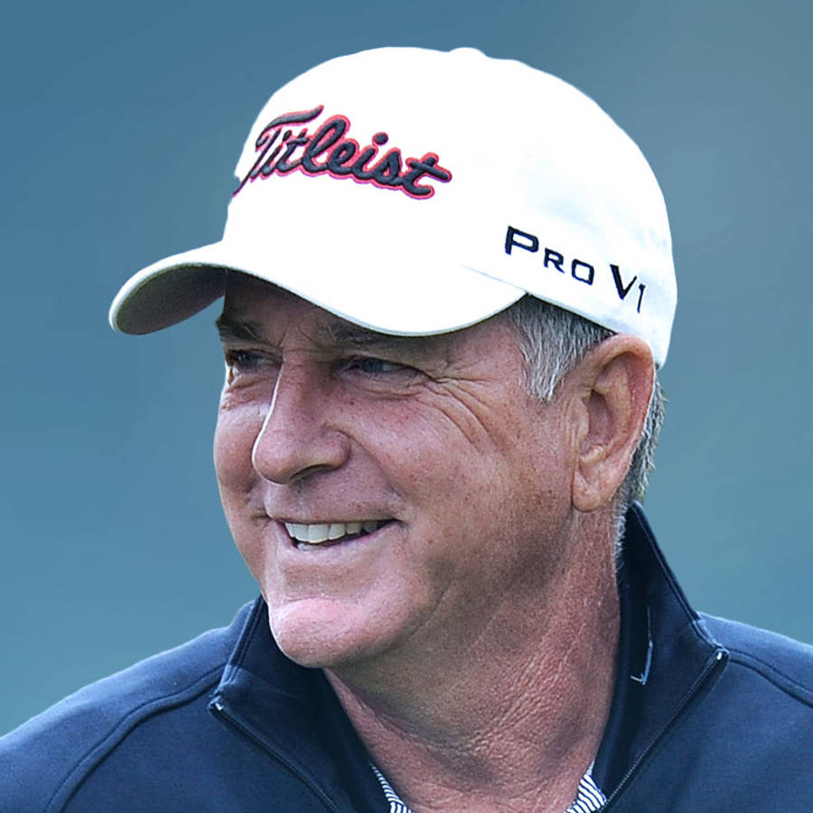 傑伊·哈斯微笑特寫 壁紙 — 一位微笑的老年男子，戴著白色Titleist Pro V1帽子，穿著深色外套，背景為柔和的藍色。