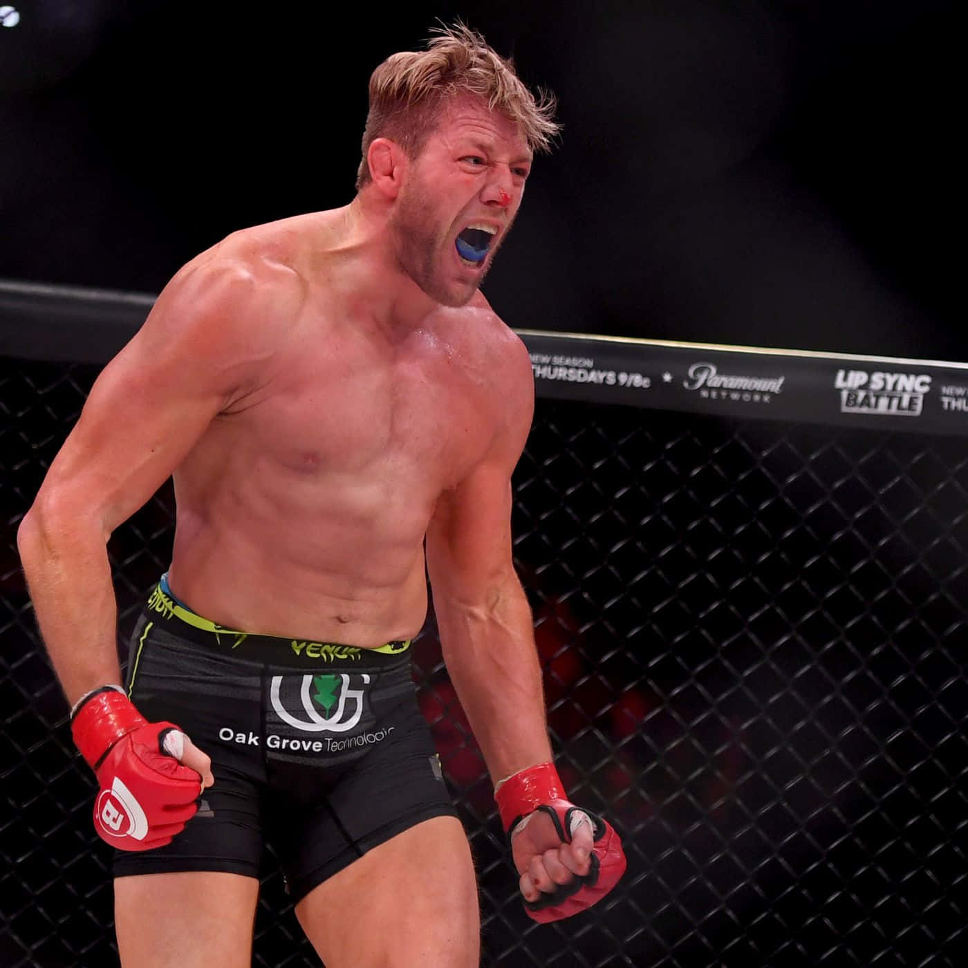 肌肉發達的戰士在MMA籠中戴著紅色手套慶祝勝利。