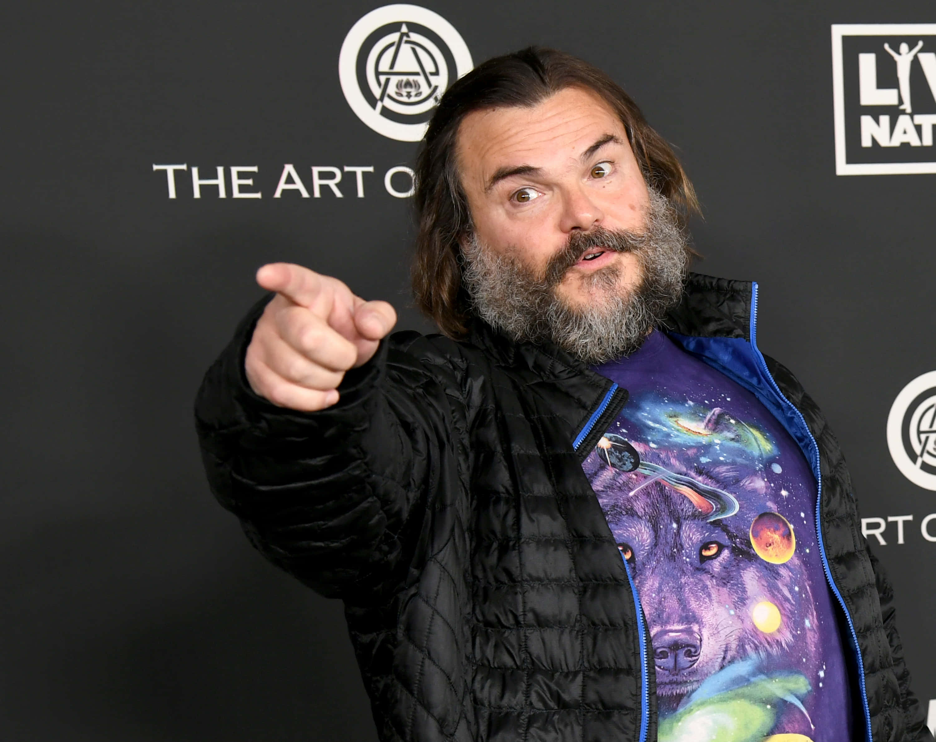 傑克·布萊克展現歡樂瞬間 壁紙 — Jack Black 露出驚訝表情向前指，在活動中穿著黑色外套內搭宇宙狼T恤。