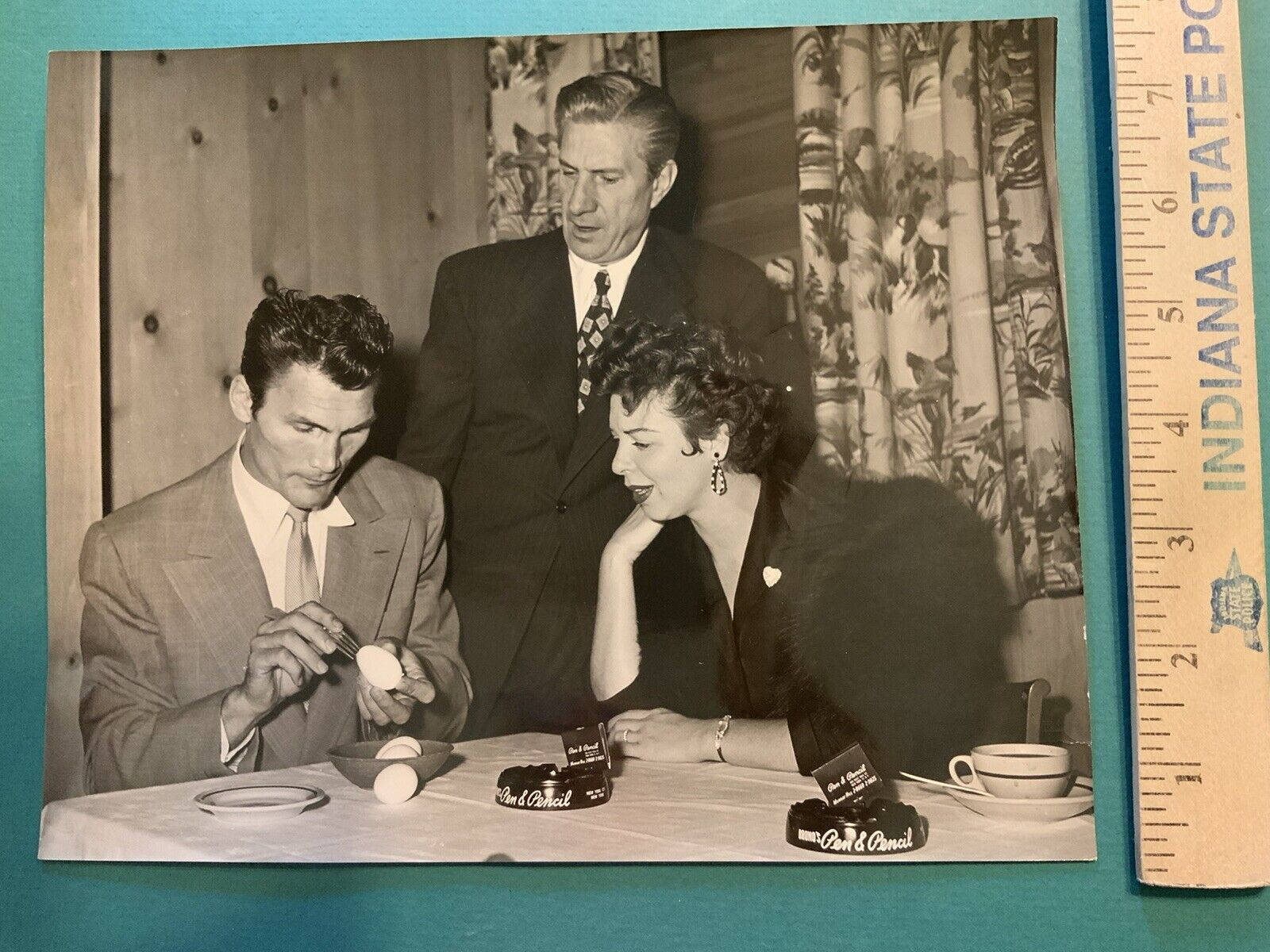 三位穿著正式的人圍繞著一張放有雞蛋和品牌物品的桌子互動。