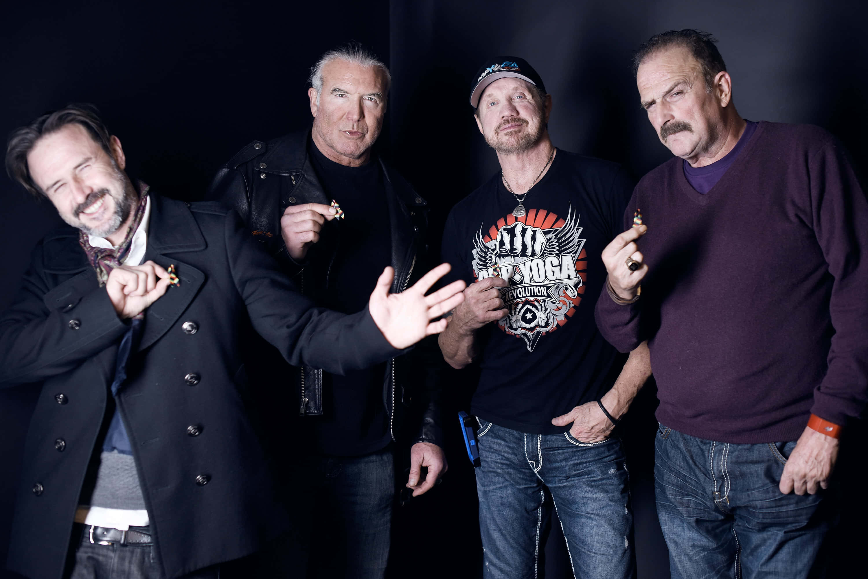 傑克·羅伯茨對抗埃博拉病毒 壁紙 — 四個身穿深色衣服的男人在黑色背景前自信地擺姿勢，每人手持一個小物件，表情俏皮。