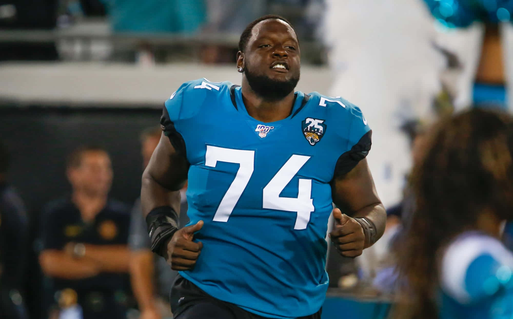 傑克遜維爾美洲虎隊74號卡姆·羅賓遜 Offensive Tackle 壁紙 — 一名身穿藍色74號球衣的傑克遜維爾美洲虎足球員在體育場燈光下比賽時專注地奔跑。