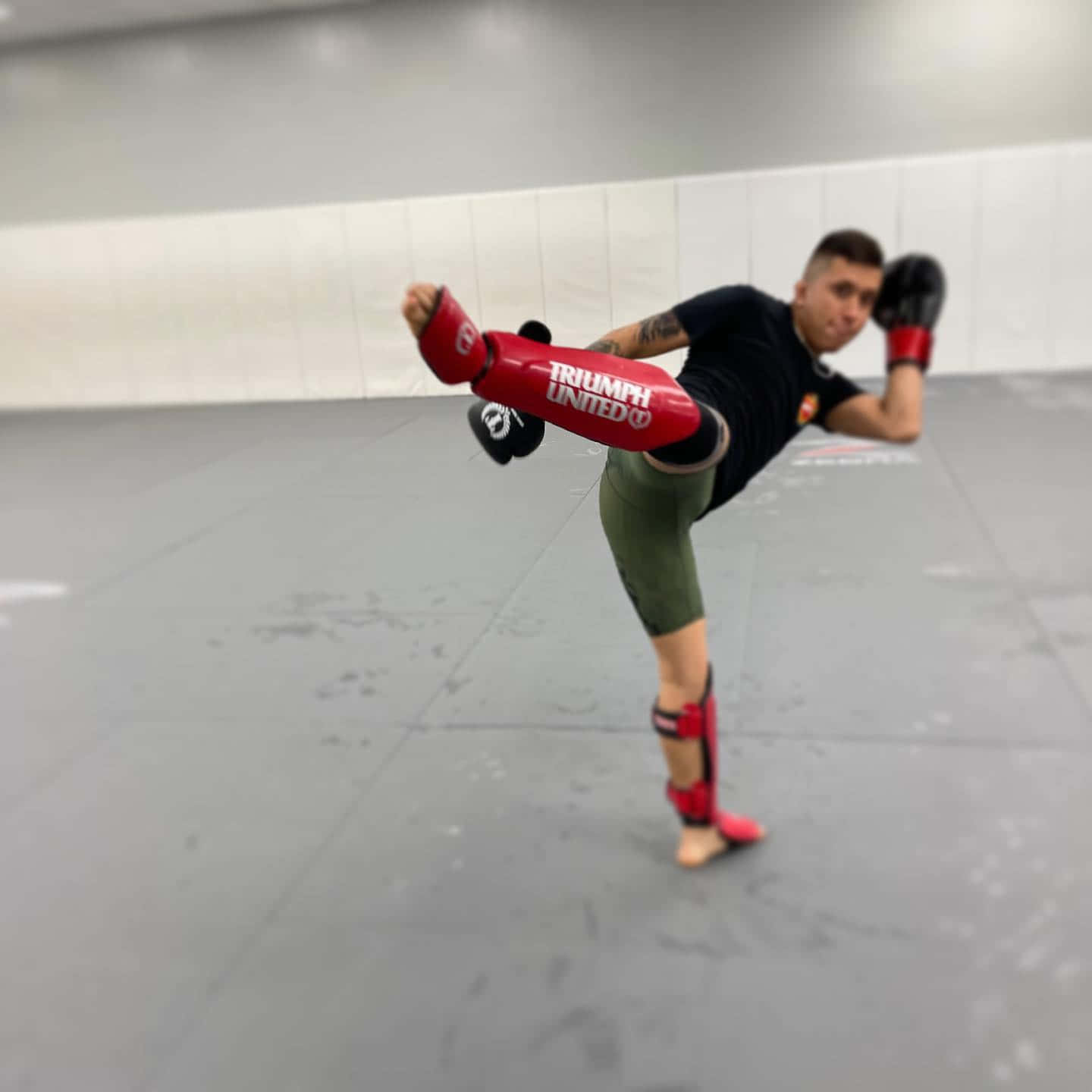 武術家在健身室內穿著紅色護脛執行高踢。