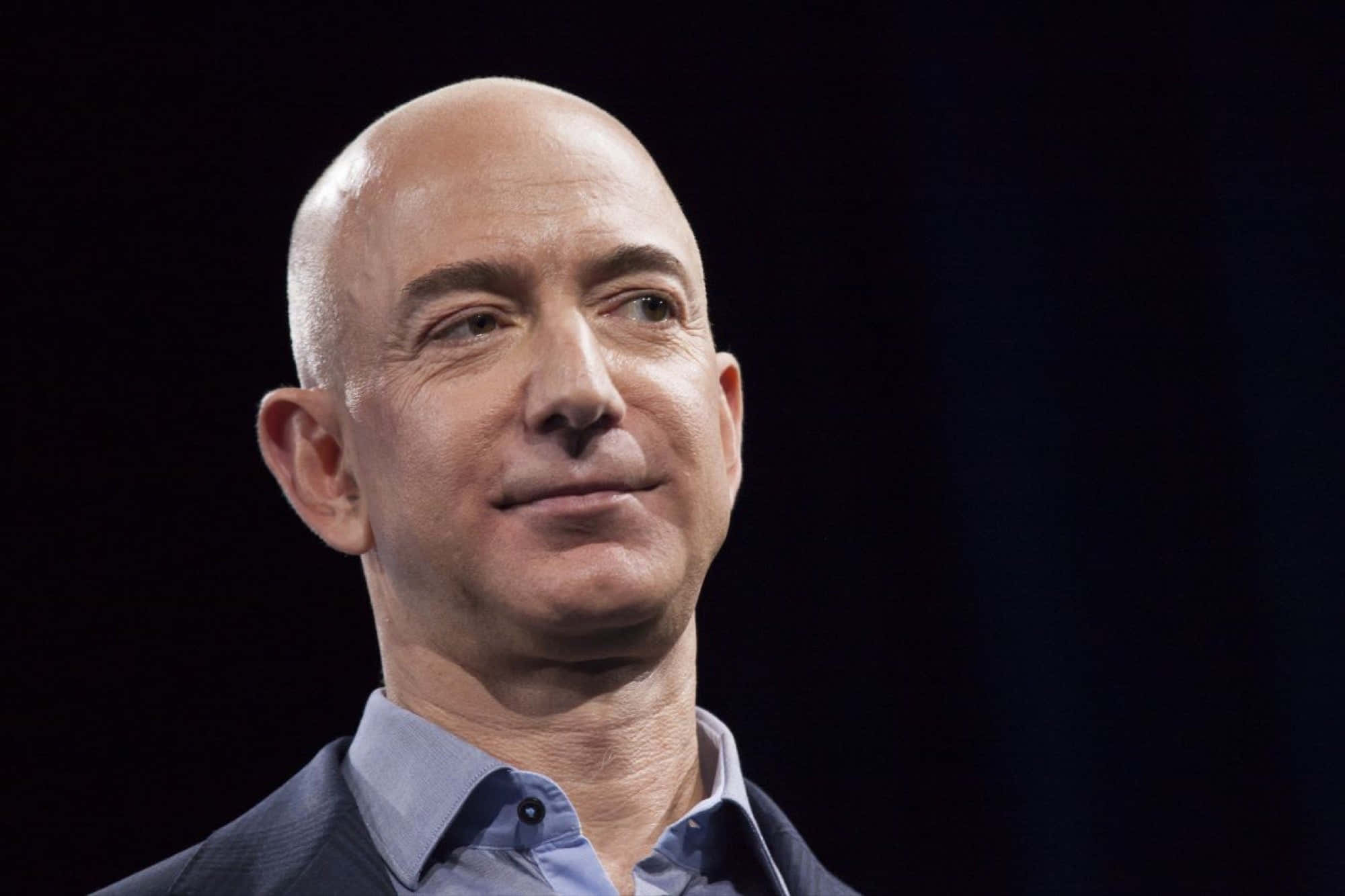 Jeff Bezos 桌布 壁紙 — 傑夫·貝索斯嘅特寫肖像，喺黑暗背景中帶柔和燈光，微微而笑。