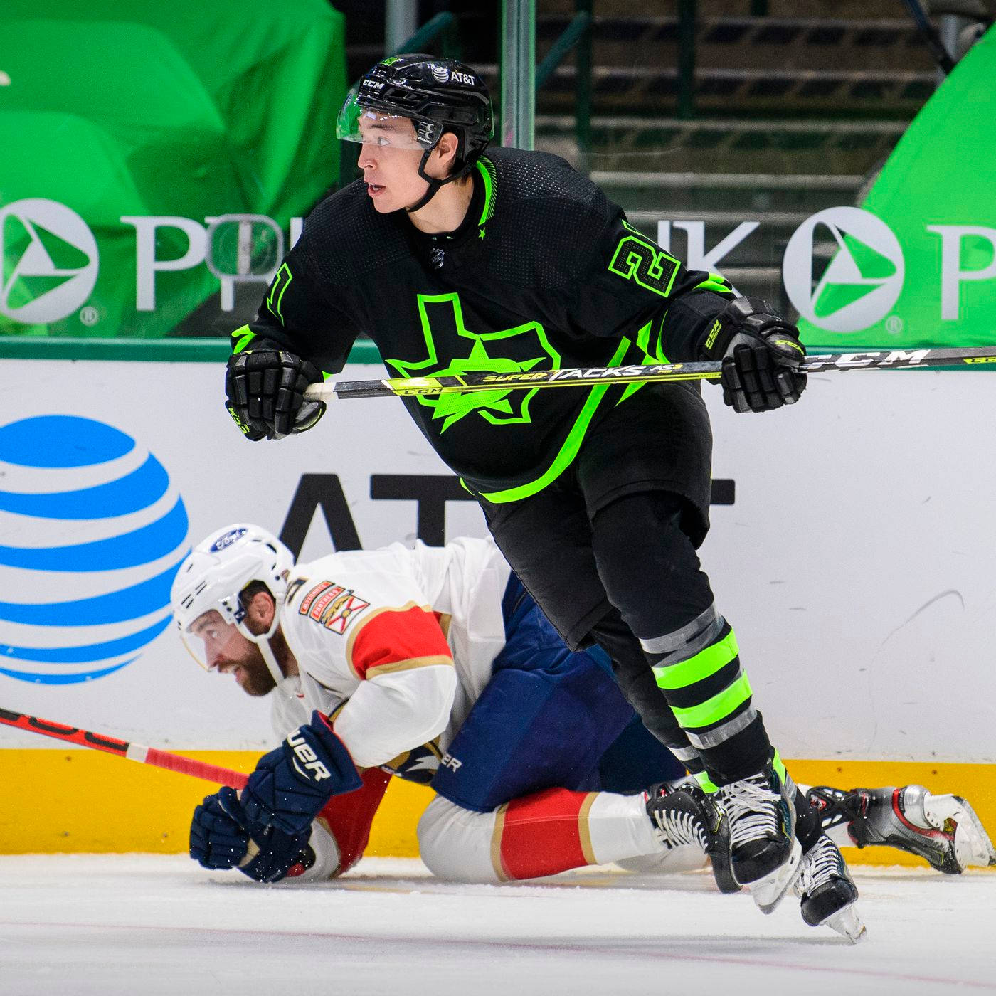 傑森·羅伯遜 Dallas Stars 對 New York Islanders 壁紙 — 一名身穿黑色和螢光綠色裝備的曲棍球選手，在帶有AT&T標誌的溜冰場上溜過一名倒地的對手。