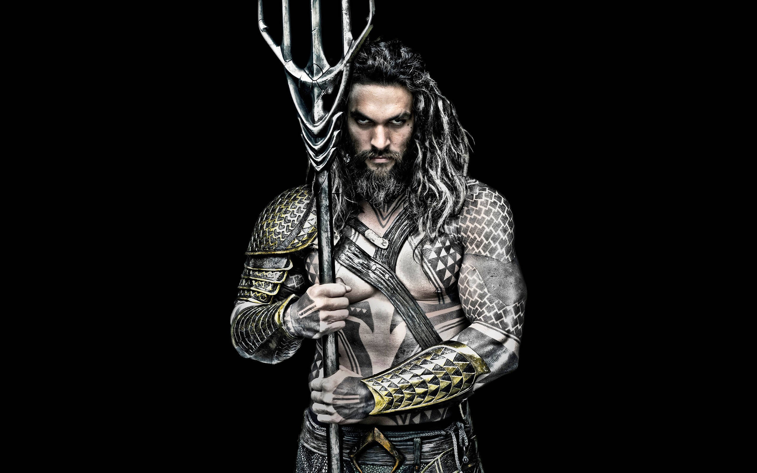傑森·莫莫亞 海王單人照 壁紙 — 一個肌肉發達、長髮鬍鬚的男子，穿著華麗的鱗甲，在黑色背景前手持三叉戟。