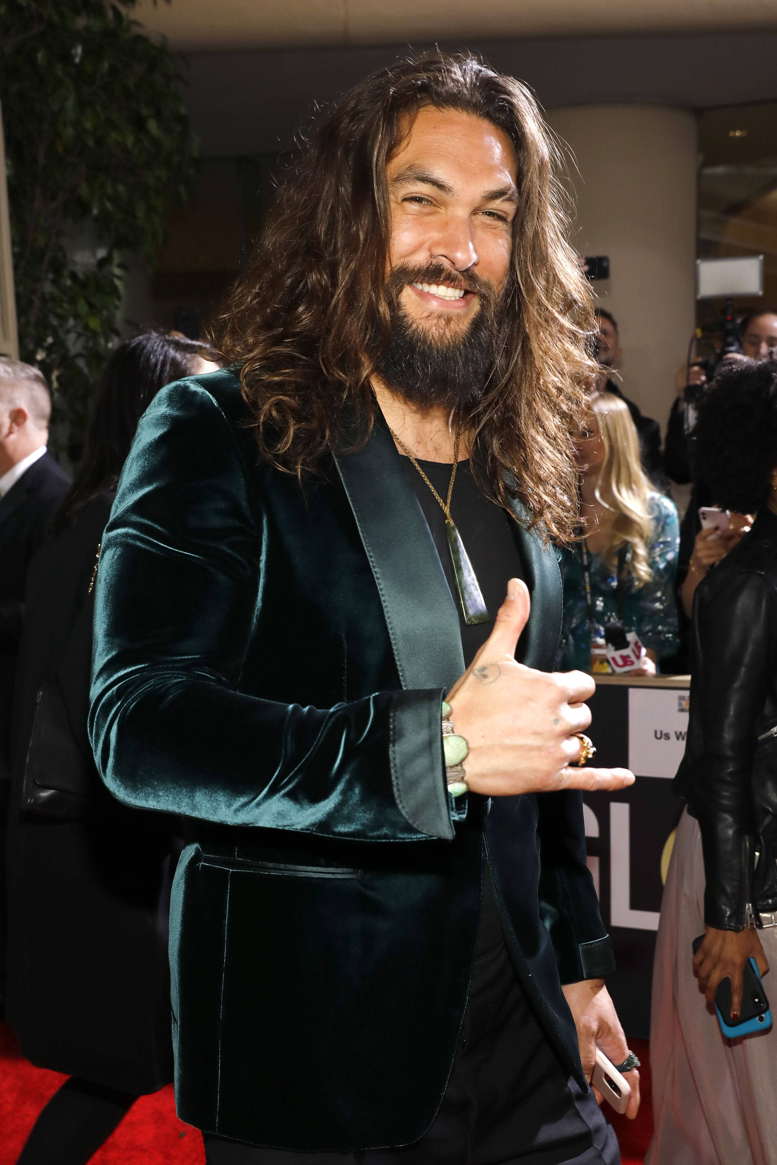 傑森·莫莫亞 紅毯 壁紙 — Jason Momoa 在紅地毯上燦爛地微笑，穿著一件毛絨的藍綠色天鵝絨西裝外套，戴著金項鍊和戒指。
