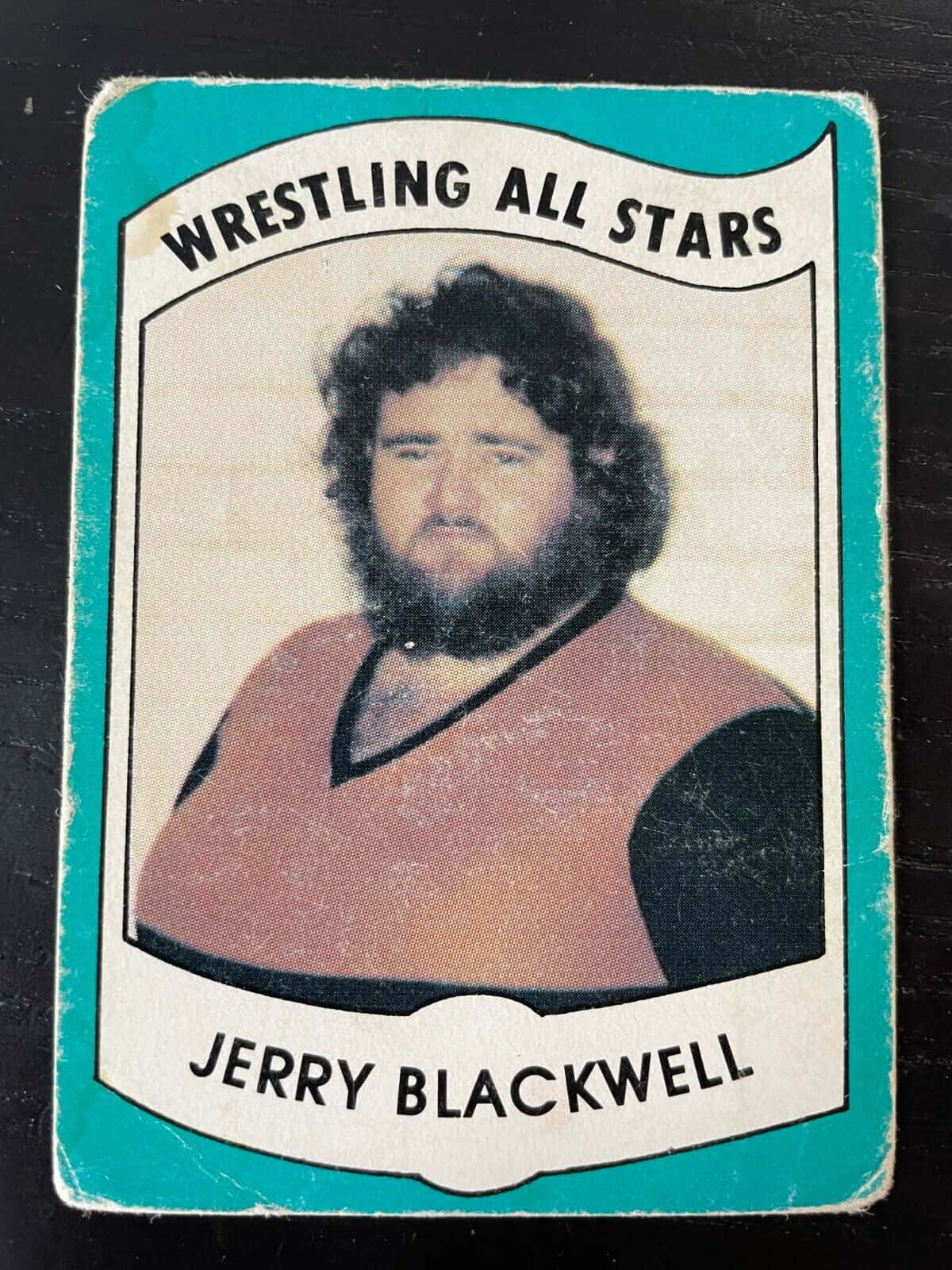 傑瑞·布萊克韋爾摔角全明星收藏卡 壁紙 — 復古摔角收藏卡， featuring Jerry Blackwell 捲髮和鬍鬚，身穿棕色和黑色背心，背景為青綠色邊框。