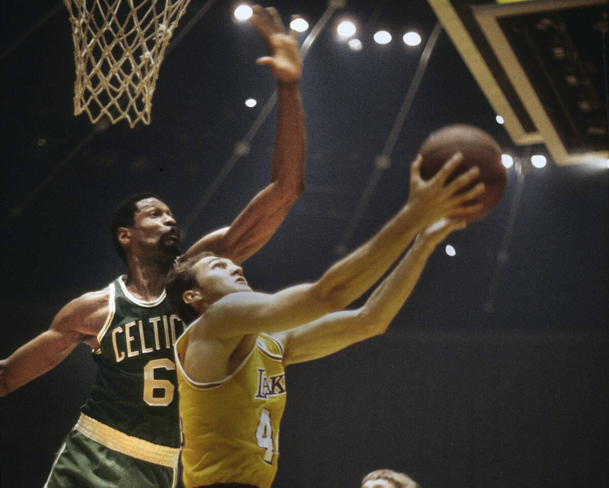 傑瑞·韋斯特對抗比爾·拉塞尔的反手上籃 1960年代NBA 壁紙 — 一位身穿黃色湖人隊球衣的籃球運動員跳向籃框，同時被一位身穿綠色塞爾特人隊球衣的球員防守。