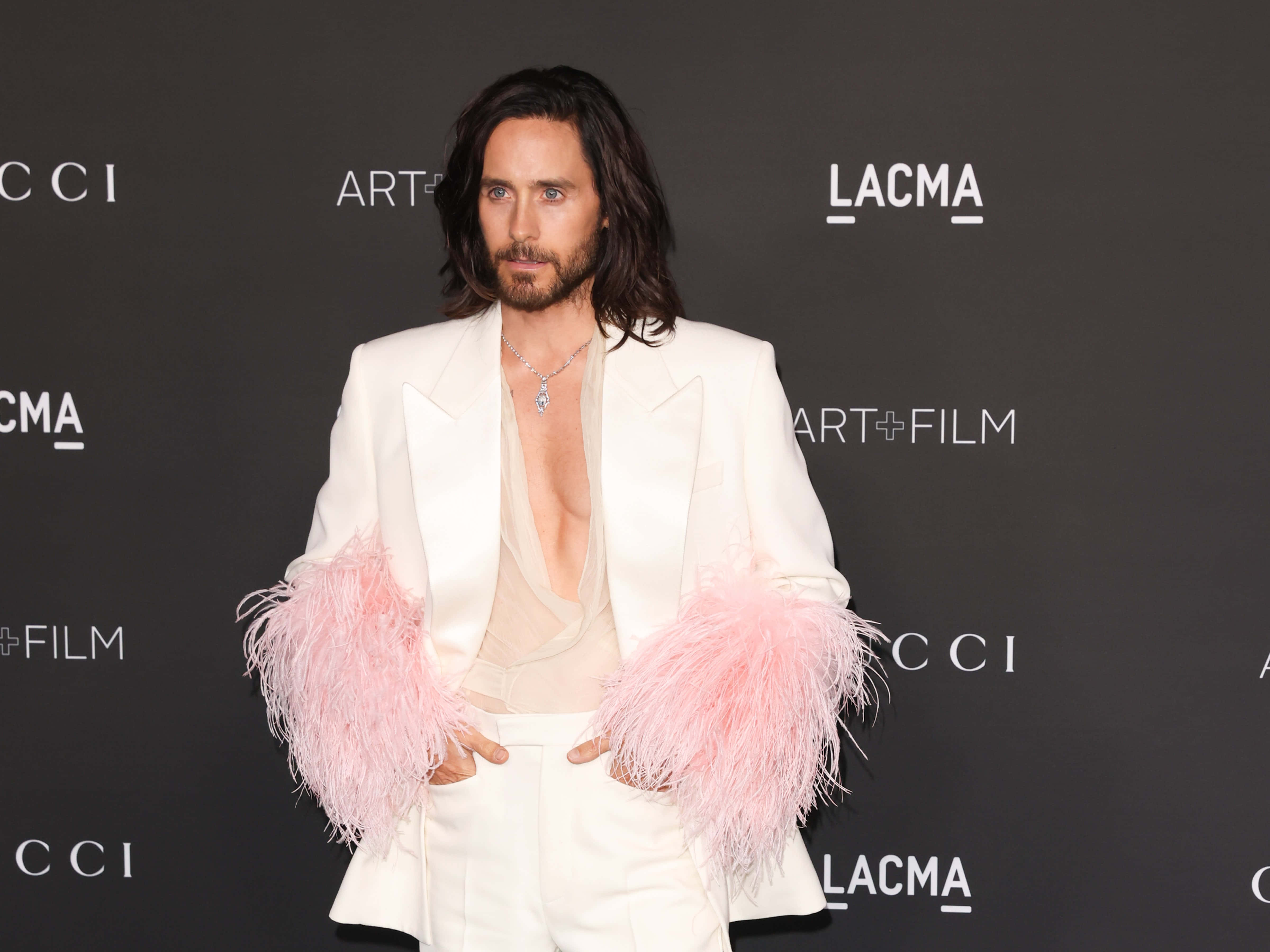 傑瑞德·雷托——演員、音樂人、製片人 壁紙 — Jared Leto 自信地穿著白色西裝，搭配粉紅色羽毛袖子，在黑色LACMA背景下擺姿勢。