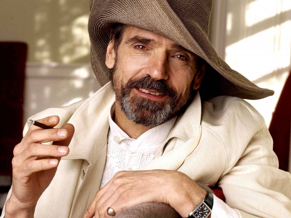 戴帽穿外套的男人在室內微笑著手持香煙。 — 古奇家族 壁紙
