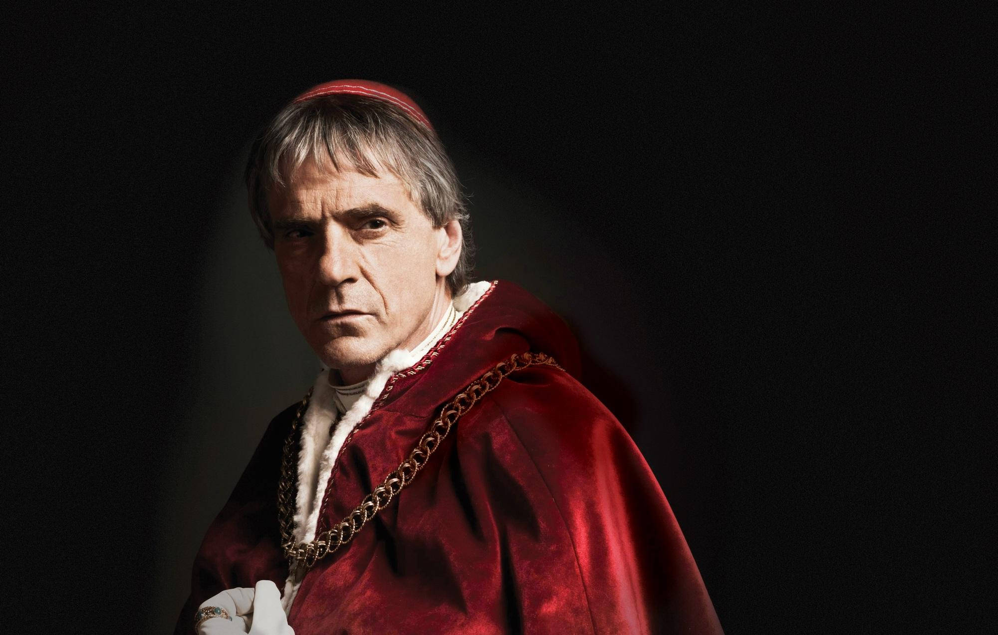 傑瑞米·艾恩斯在《波吉亞家族》電影中 壁紙 — 一位莊嚴的男子身穿紅色天鵝絨教皇長袍和朱凱托帽，站在黑暗背景前，燈光效果戲劇化。