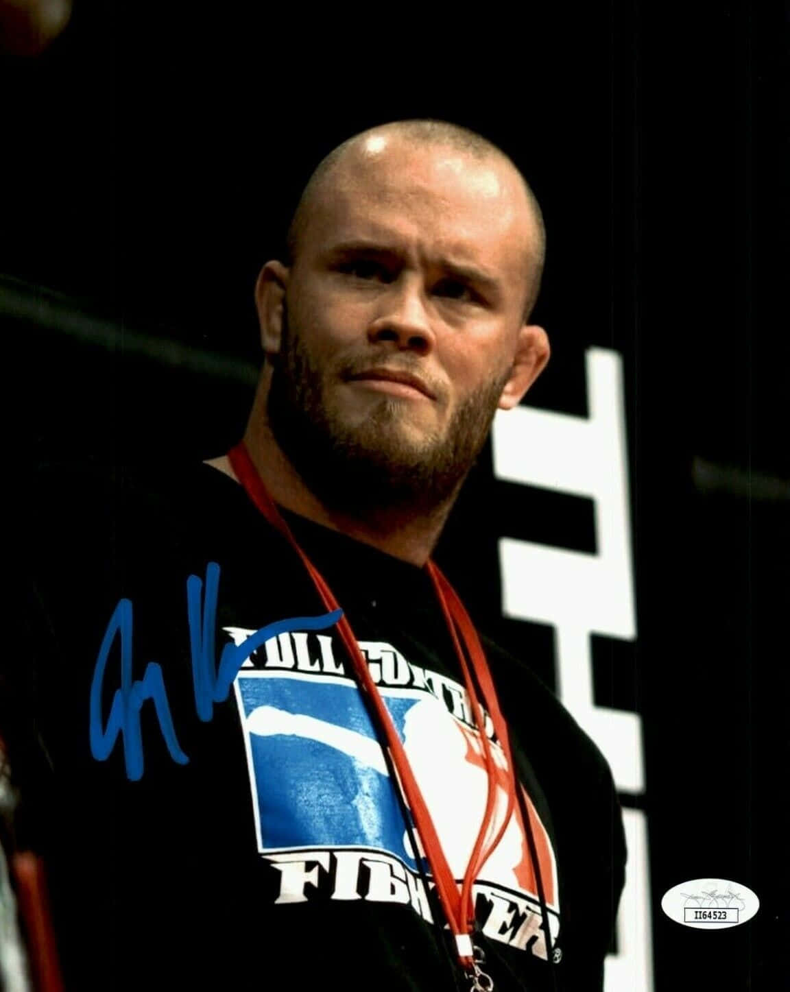傑瑞米·霍恩UFC入場高畫質 壁紙 — 一位光頭鬍鬚戰士穿著黑色「Full Contact Fighter」襯衫，配紅色掛繩，在帶有白色幾何形狀的深色背景下凝視著。