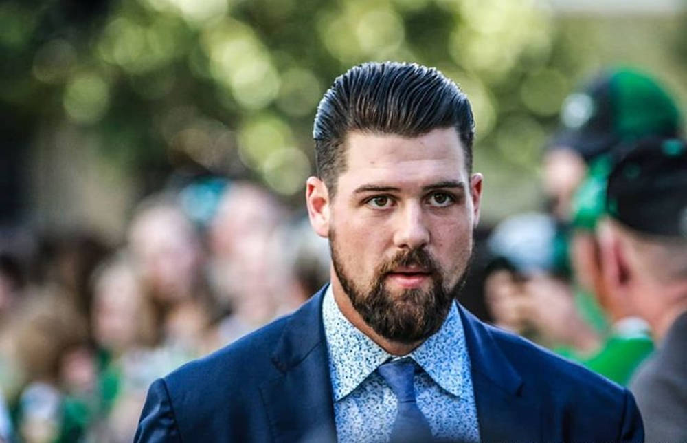 傑米·本恩身穿西裝的NHL球員 壁紙 — 一位男士擁有時尚髮型和鬍鬚，身穿藍色西裝和圖案襯衫，站在戶外，背景是模糊的綠植和人羣。
