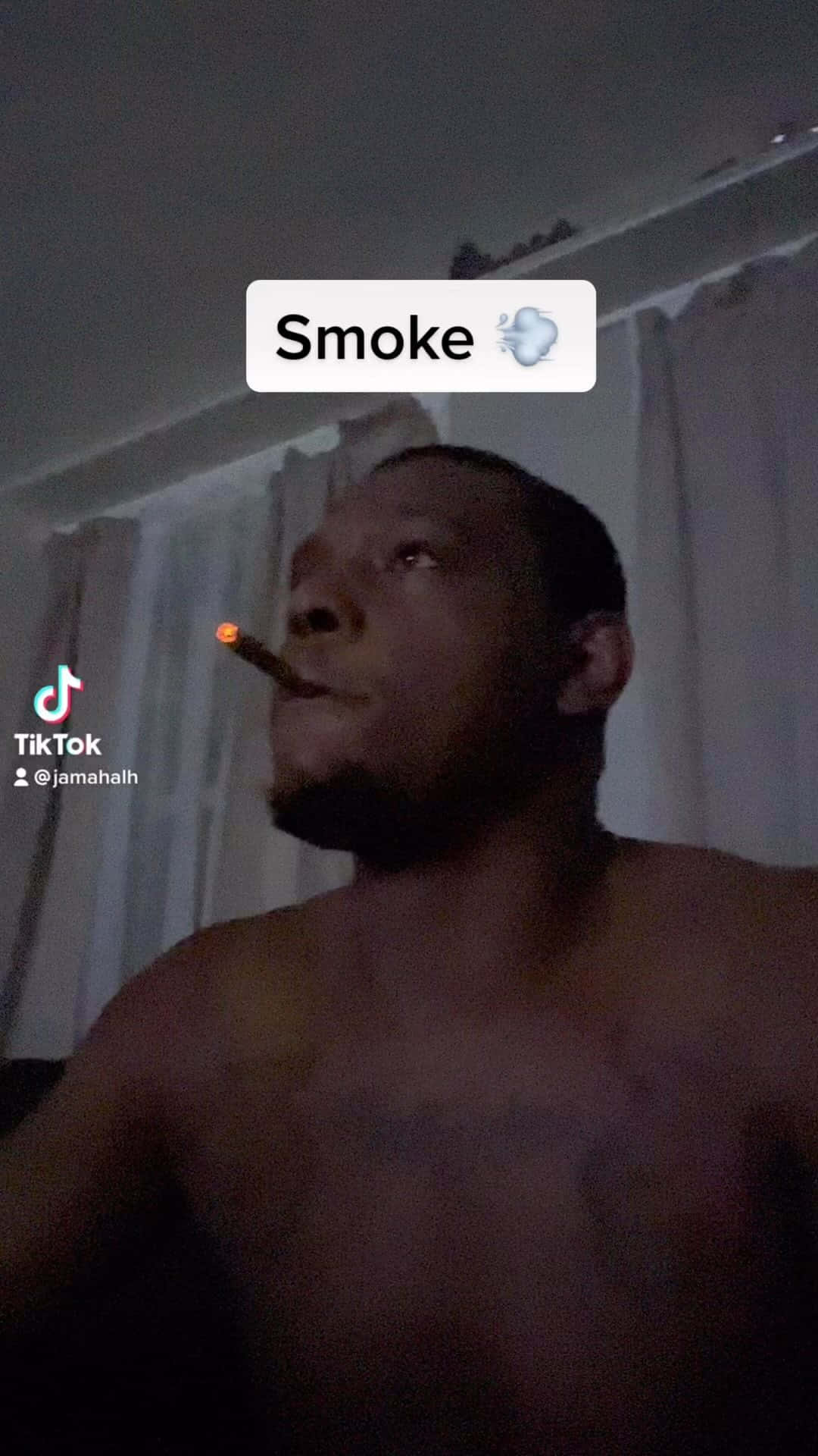 一名赤裸上身的男子在夜間於室內抽著點燃的雪茄煙。