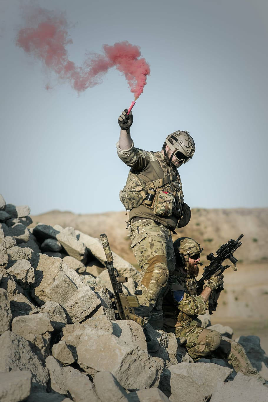 兩名士兵在沙漠地形中使用紅色煙霧信號彈進行信號傳遞。