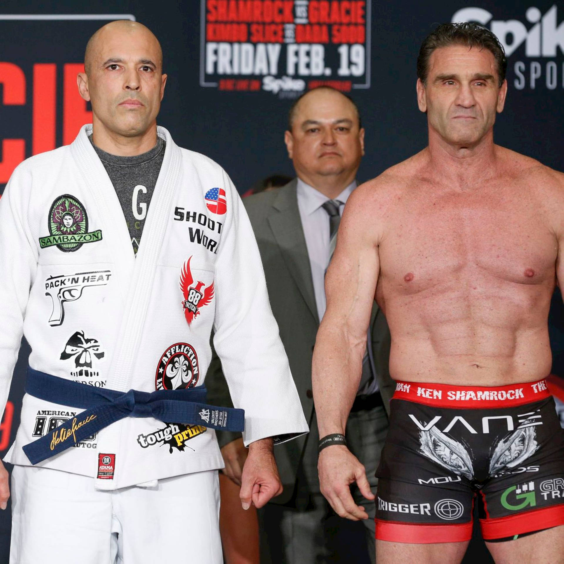 兩名男性MMA拳手在稱重活動中，一人身穿白色道服，另一人身穿黑色短褲。