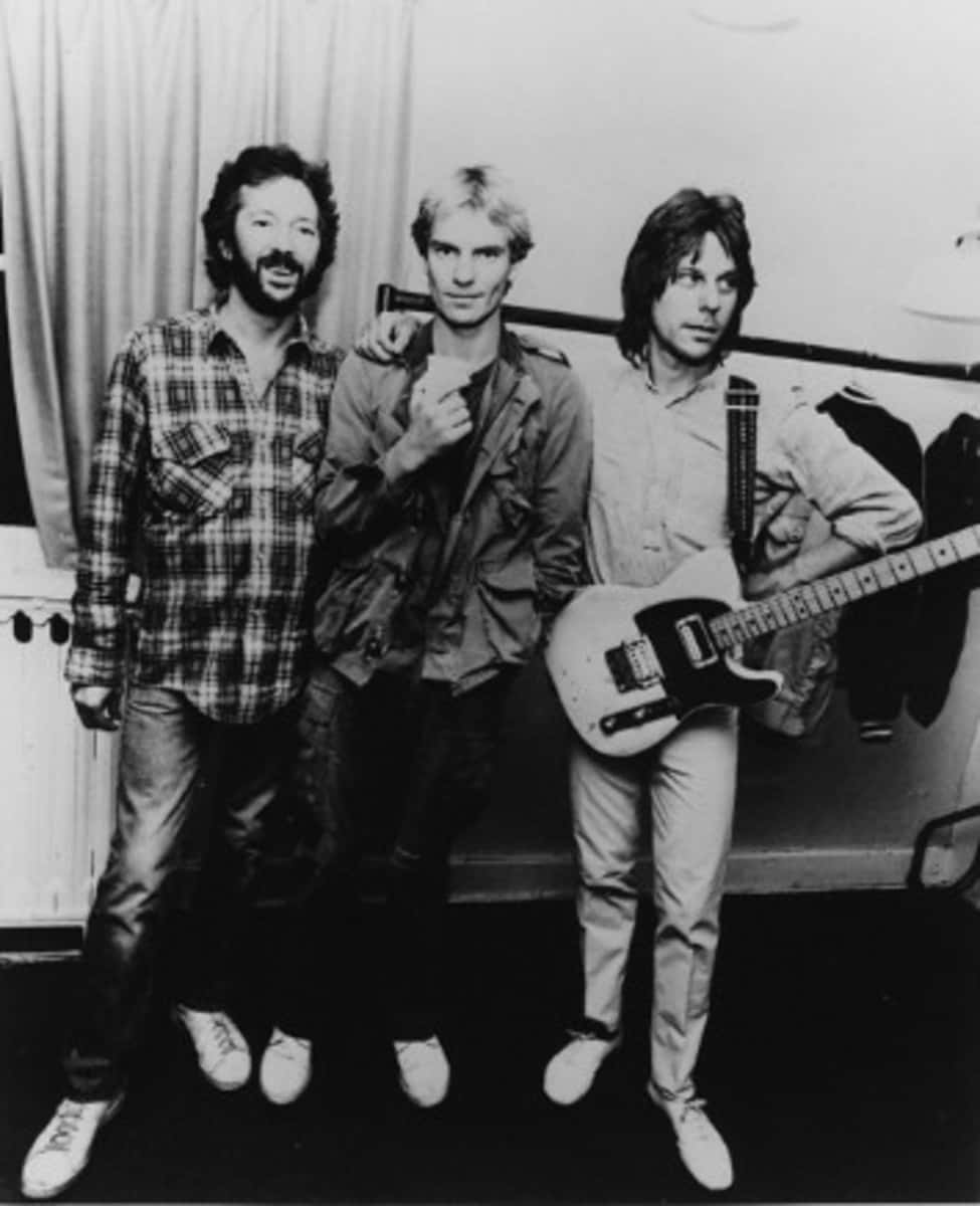 傳奇 Yardbirds 成員 Eric Clapton、Sting 與 Jeff Beck 的經典時刻 壁紙 — 三位男士身穿復古休閒服裝，在純色背景前自信地拿著結他擺姿勢的黑白照片。