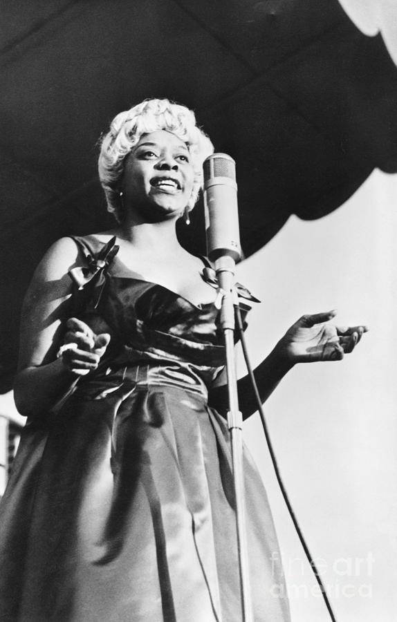 傳奇Dinah Washington的復古輝煌 壁紙 — 一位微笑女士穿著華麗連衣裙對著復古麥克風唱歌的黑白照片。