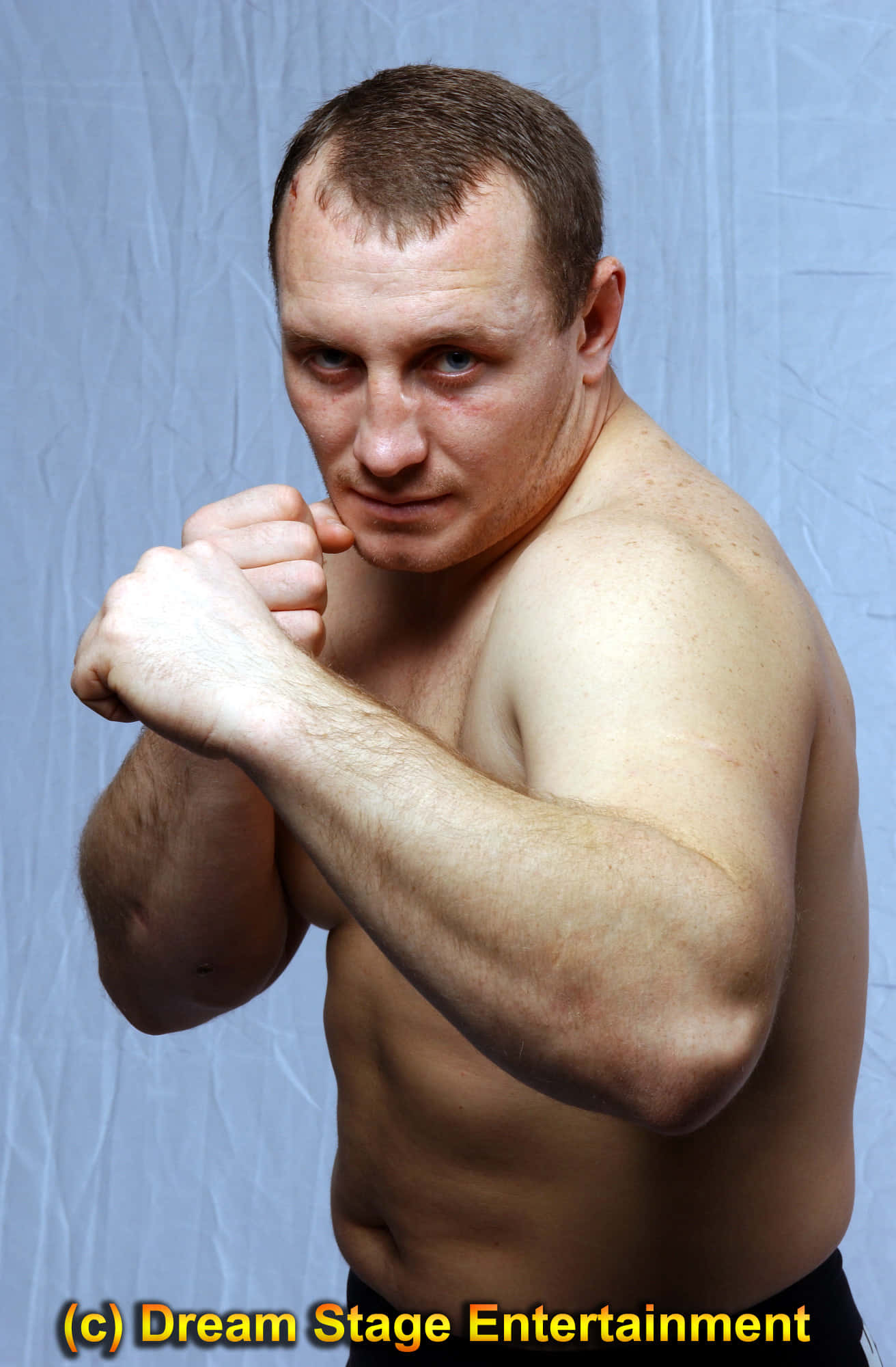 傳奇MMA選手伊戈爾·沃夫恰寧 壁紙 — 一個肌肉發達、赤裸上身的男子以戰鬥姿勢，對著皺巴巴的藍色背景凝視。