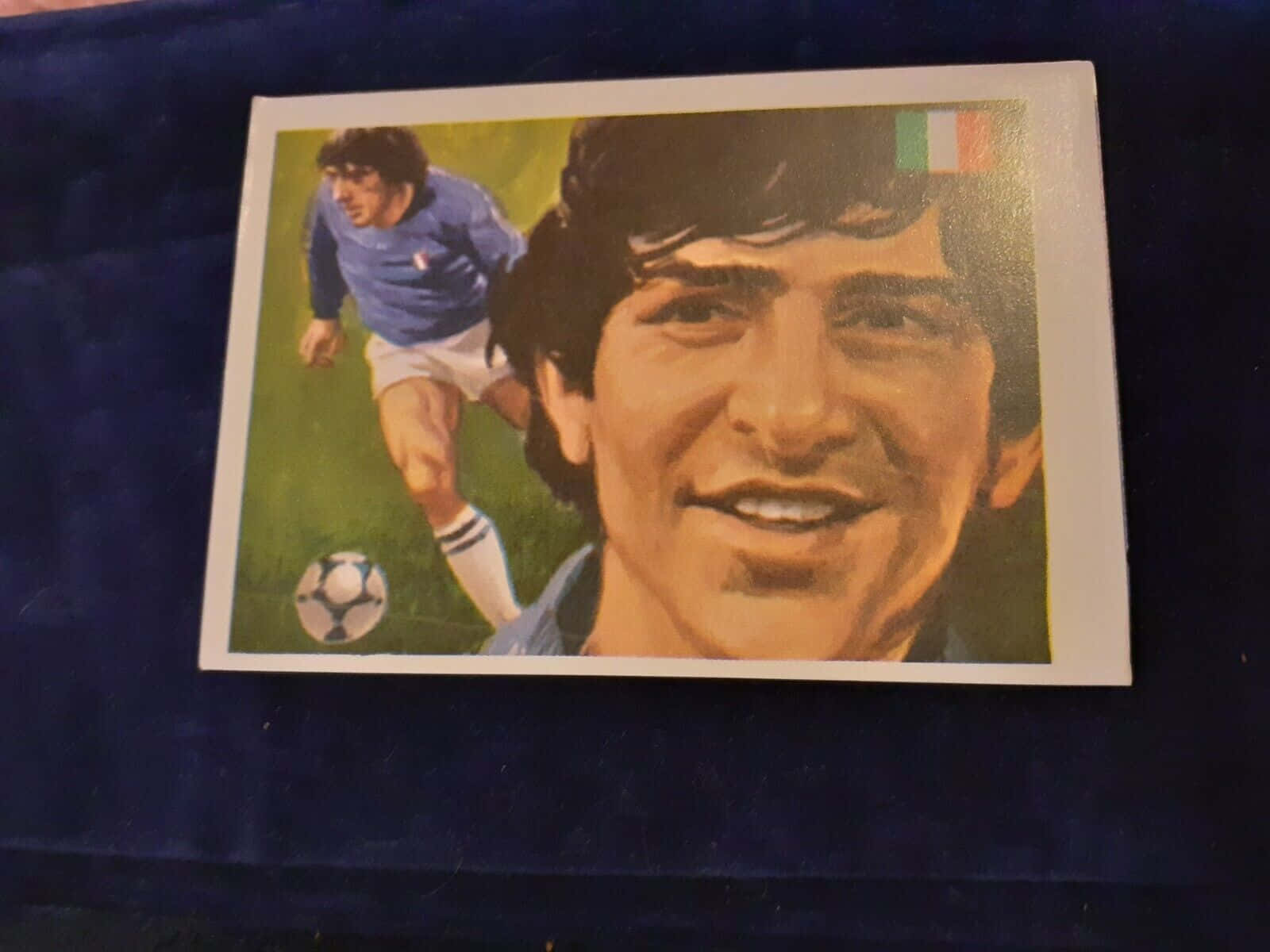 傳奇意大利足球員 Paolo Rossi 壁紙 — 復古足球交換卡，展示一位微笑的球員身穿藍色球衣，頭頂意大利國旗，背景為動作鏡頭。