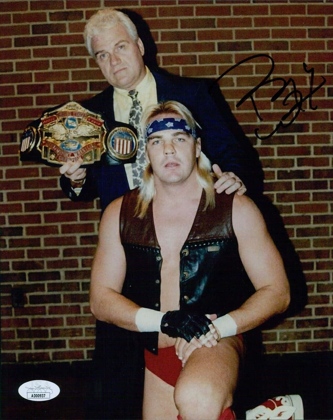 傳奇摔角手Barry Windham與經典經理J.J. Dillon 壁紙 — 兩名摔角手在磚牆前擺姿勢，一人手持冠軍腰帶，另一人穿著皮革裝備跪地。