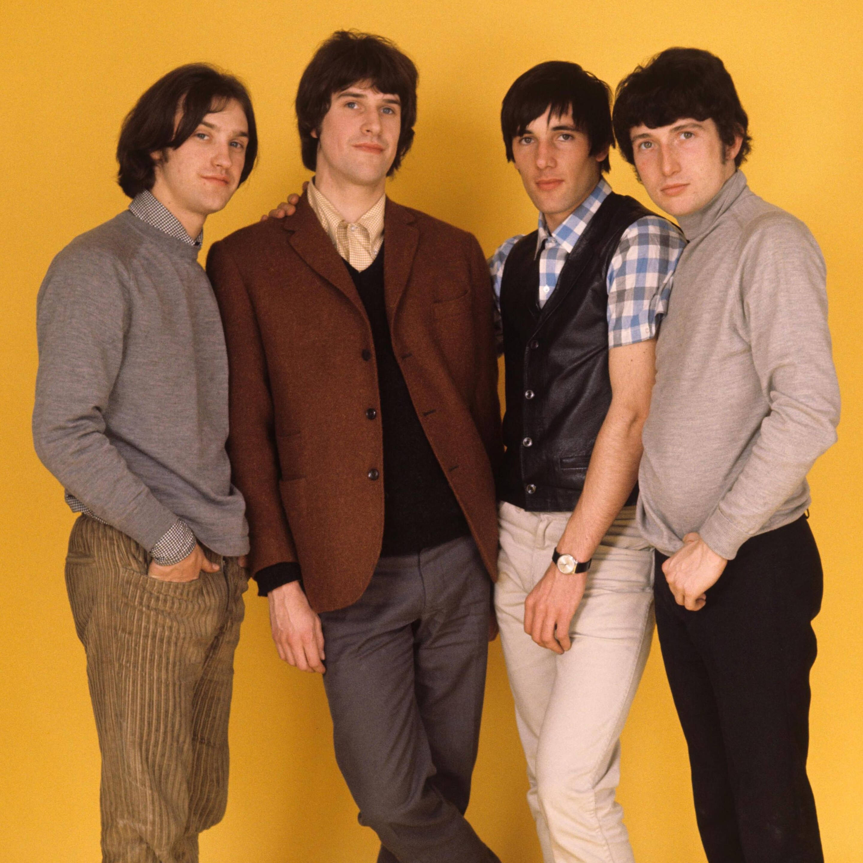 傳奇樂隊 The Kinks 的經典拍攝照 壁紙 — 四位身穿1960年代時尚的年輕男子在純黃色攝影棚背景前自信地擺姿勢。