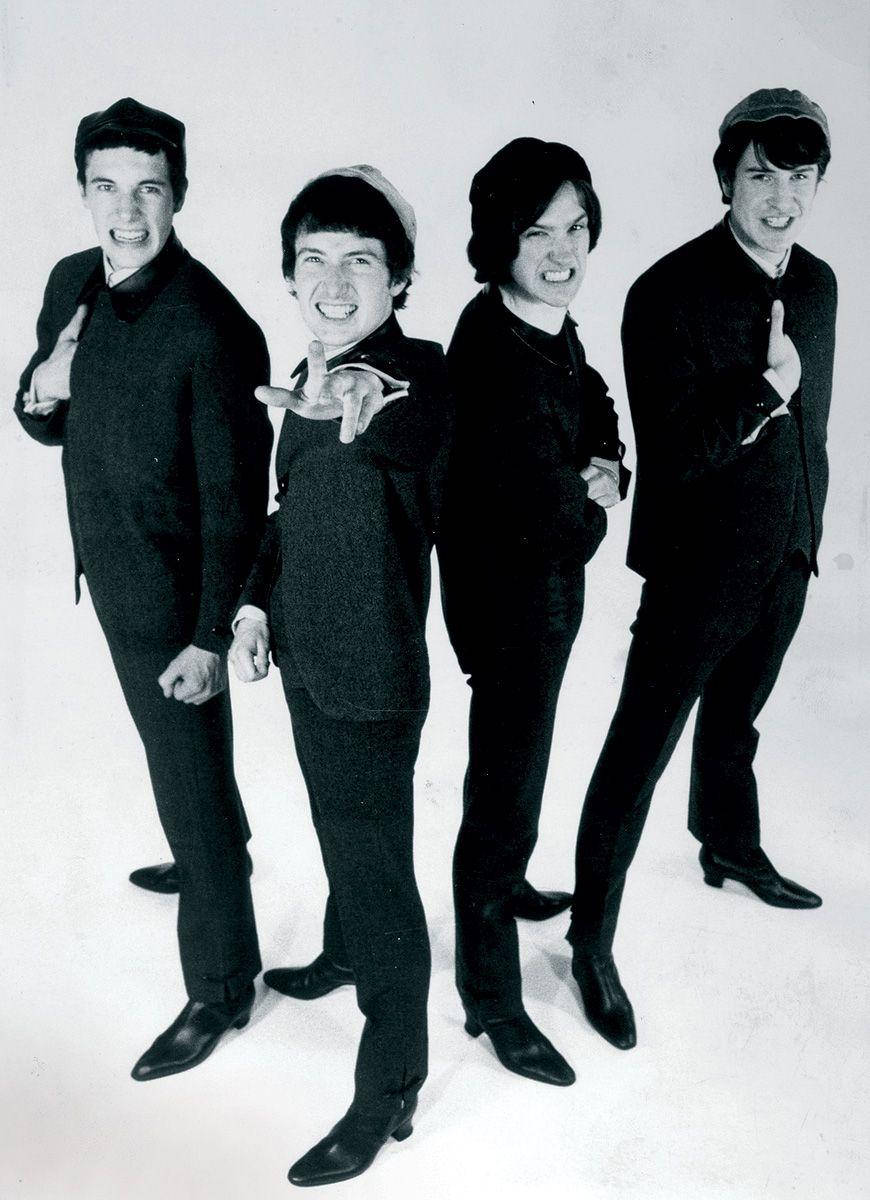 傳奇樂隊The Kinks的成員 壁紙 — 四位年輕男士身穿相配的深色西裝和帽子，在純白色背景前以俏皮的表情充滿活力地擺姿勢。
