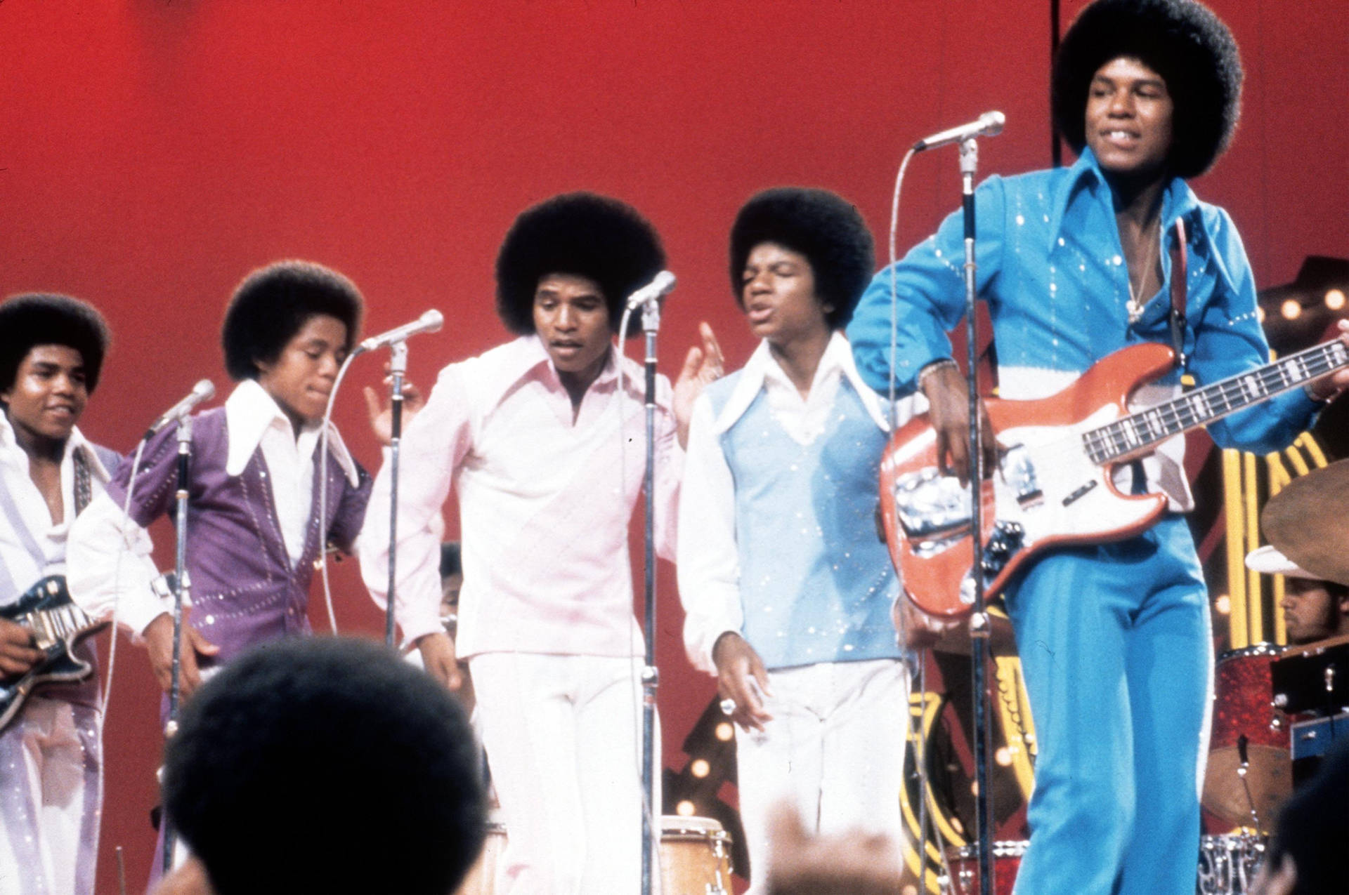Jackson Five 在舞台上穿著色彩繽紛的70年代服裝，手持麥克風和結他現場表演。