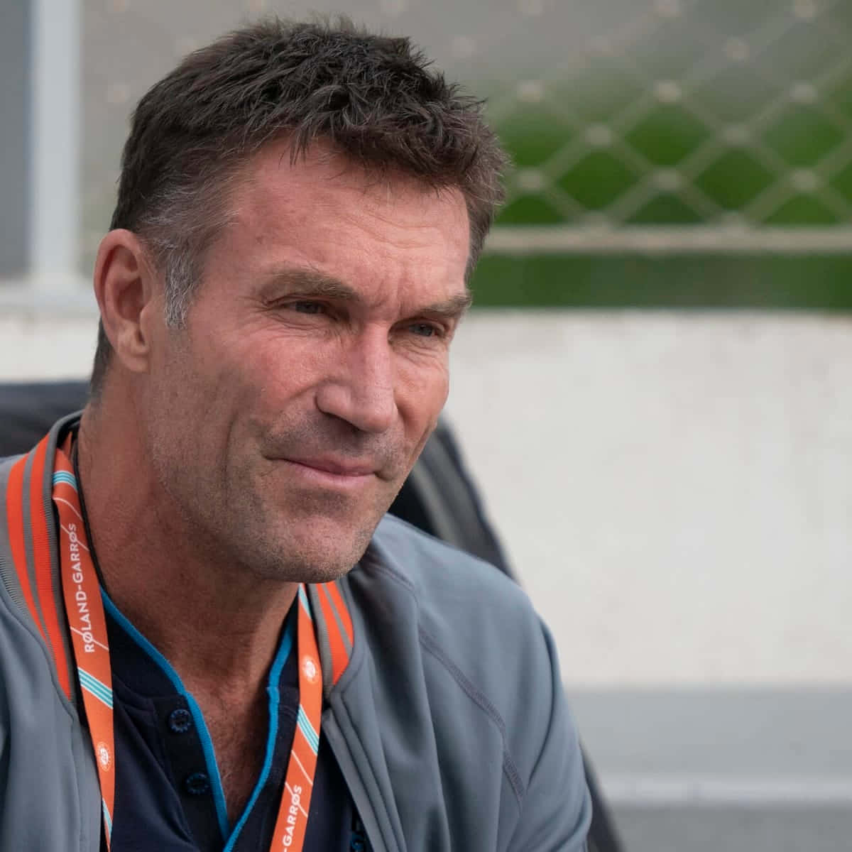 傳奇網球手 Pat Cash 賽場專注瞬間 壁紙 — 一名短黑髮、面帶微笑的男子近照，佩戴Roland-Garros掛繩。