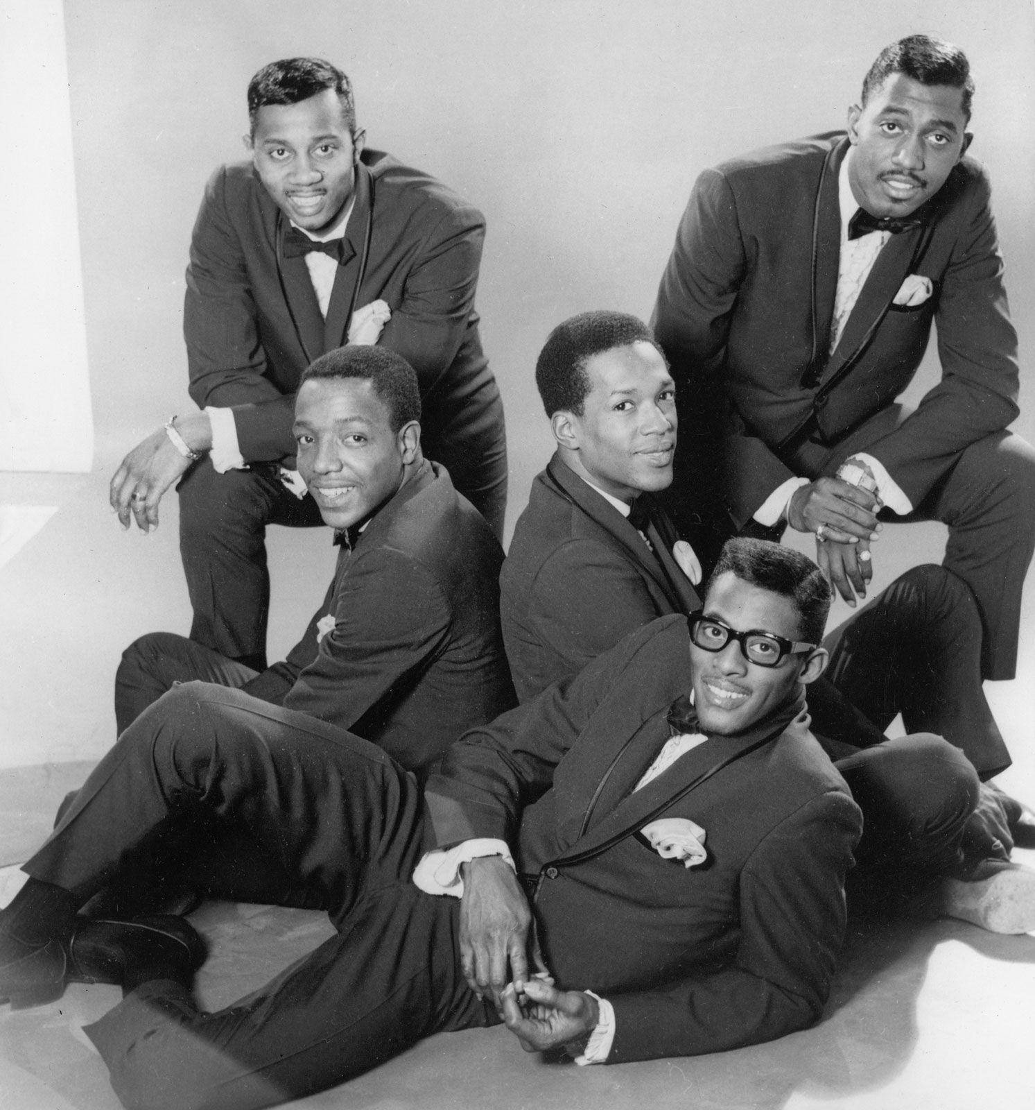 傳奇美國演唱組合 - The Temptations（1966） 壁紙 — 五位穿著時尚西裝的男士在素色地板上，以中性背景自信地擺出姿勢，呈現經典黑白工作室肖像。