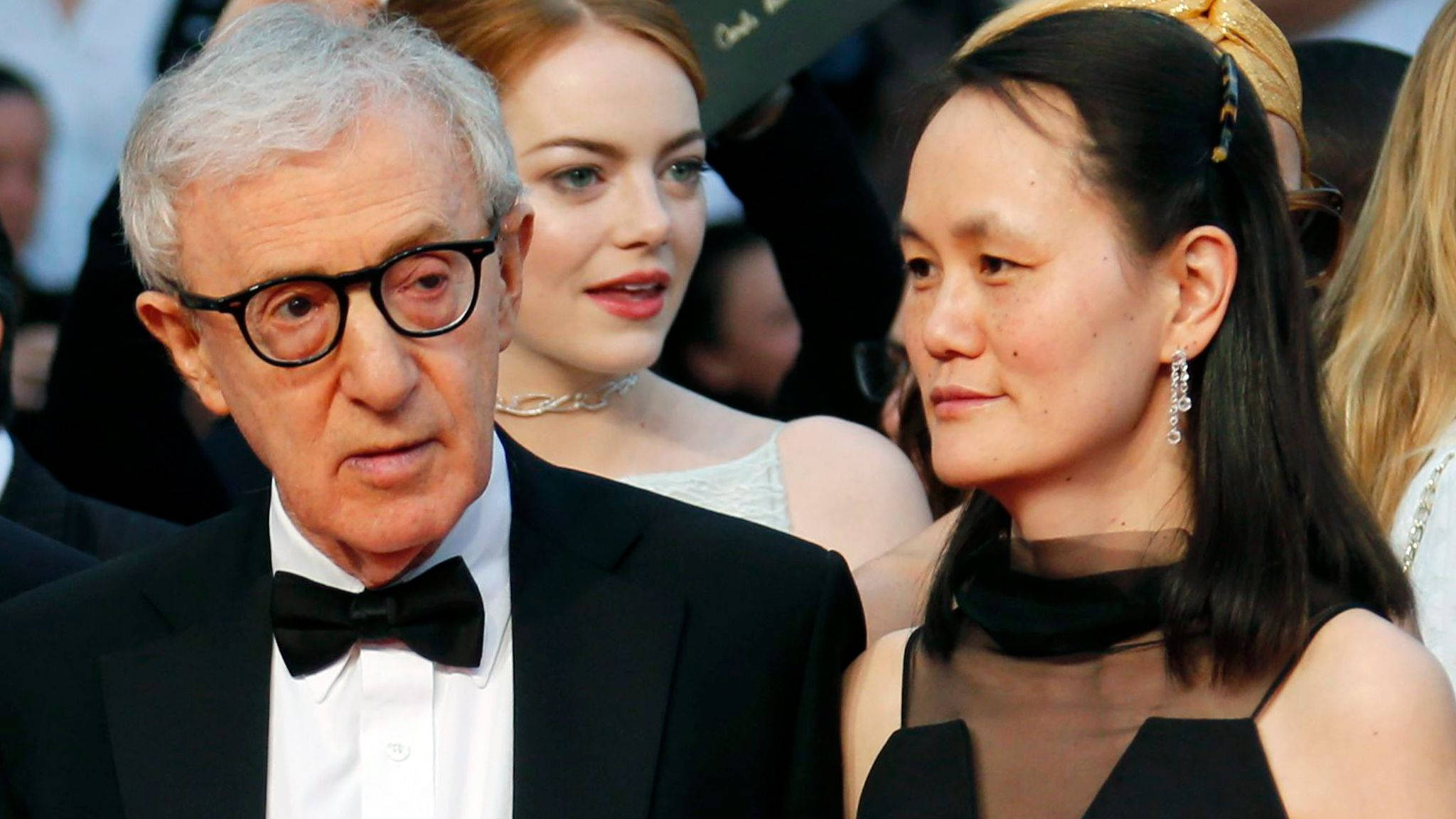 傳奇美國電影導演伍迪·艾倫與妻子蘇茵·普雷文 壁紙 — Woody Allen 身穿黑色禮服和領結，站在一位身穿黑色連衣裙的女性旁邊，在一個華麗的紅地毯活動中。