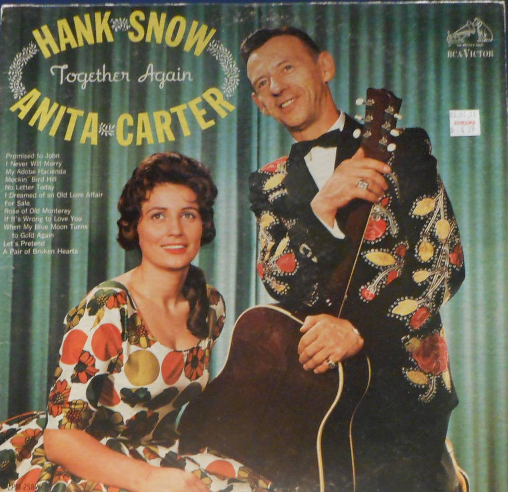 傳奇鄉村歌手漢克·斯諾與阿妮塔·卡特同台演出 壁紙 — Hank Snow 和 Anita Carter 穿著復古花卉服裝，在經典 RCA Victor 專輯封面上，以綠色窗簾為背景，溫暖地微笑。