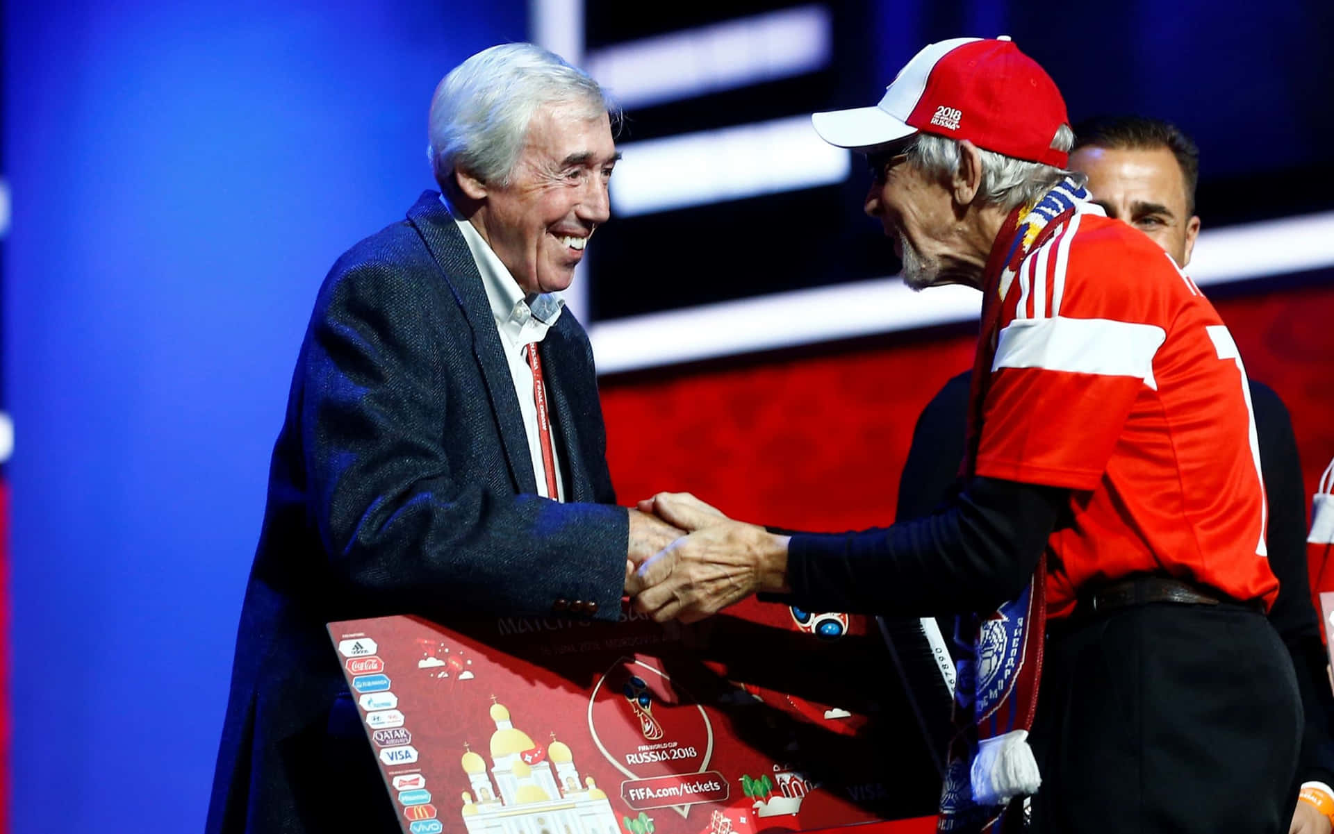 兩名男子在FIFA世界盃活動中在紅色講台上握手。