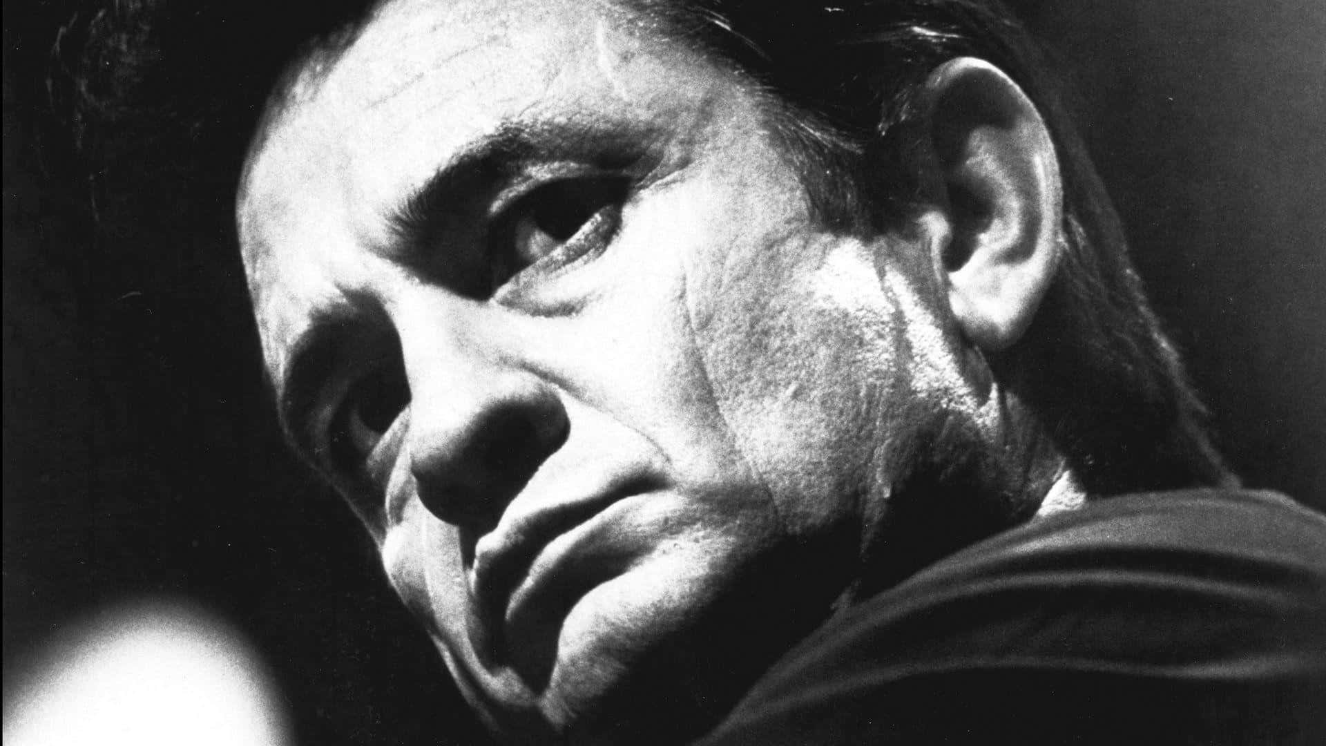 傳奇音樂人 Johnny Cash 壁紙 — 一個戲劇性的黑白特寫，展示一個男人飽經風霜的臉龐，在黑暗背景下被強烈燈光照亮。
