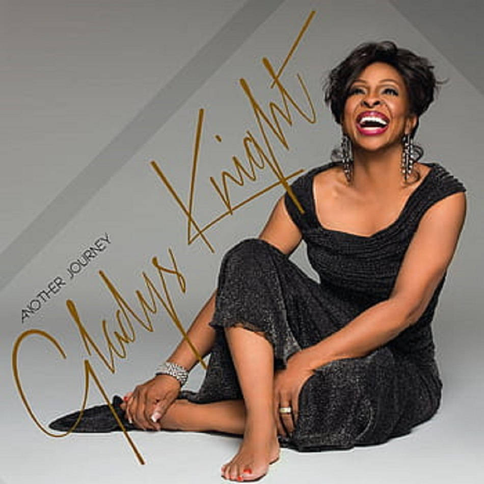 傳奇音樂團體——格拉迪斯·奈特與合唱團 壁紙 — Gladys Knight 赤腳坐在錄音室地板上，穿著閃亮黑色連衣裙，上面有金色文字覆蓋，開懷大笑。