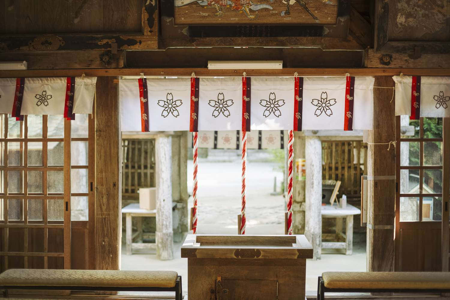 Japanese 桌布 壁紙 — 傳統日本神社內部，木造建築，白色簾幕上有神聖的櫻花圖案。