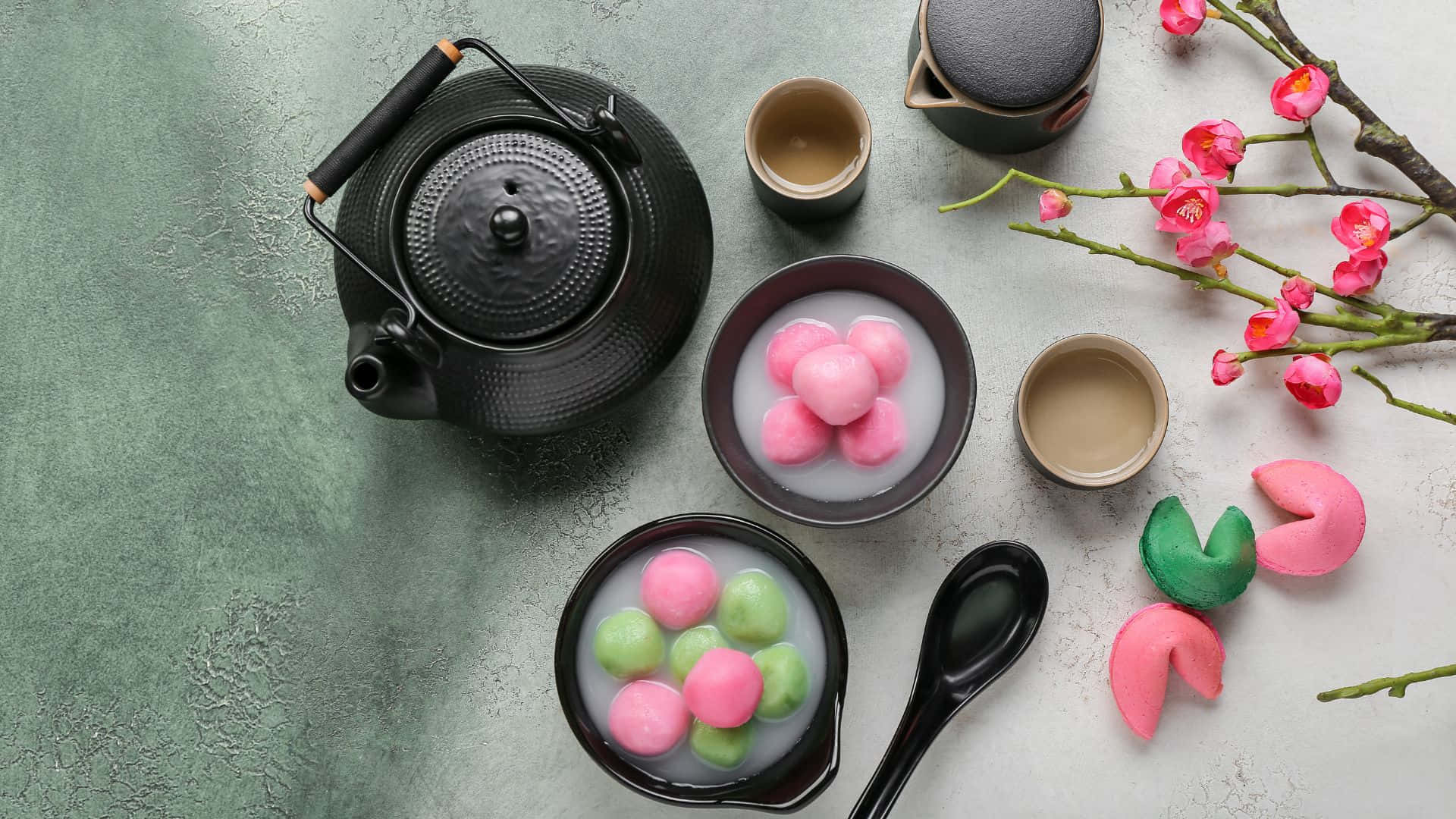 傳統湯圓甜點 壁紙 — 傳統日本茶具套裝的俯視圖，碗中有粉紅色和綠色的麻糬糰子，旁邊有櫻花枝。