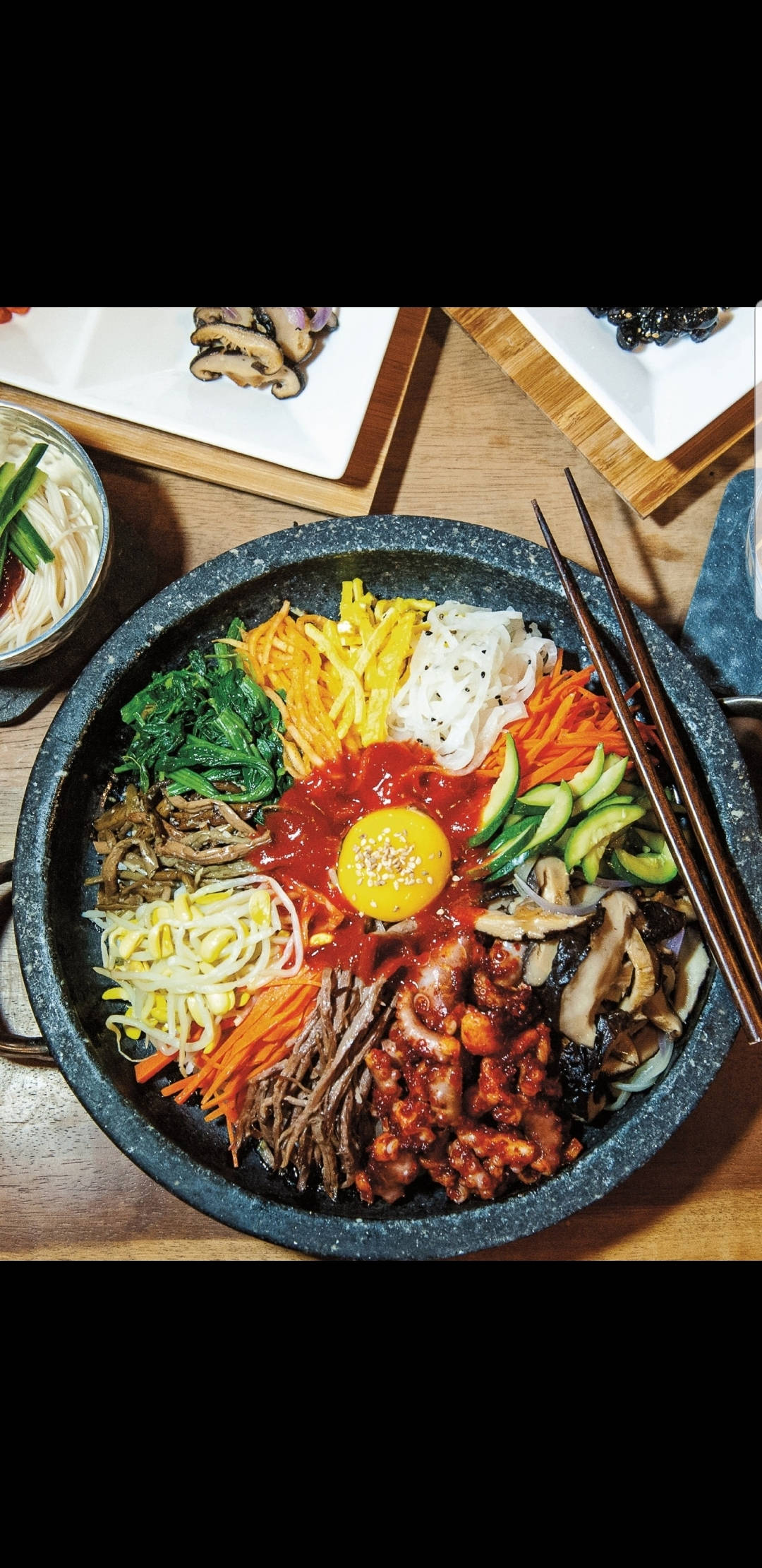 傳統韓式拌飯擺盤方式 壁紙 — 一個充滿活力的韓國石鍋拌飯，上面放著太陽蛋和色彩繽紛的蔬菜，放在木桌上。