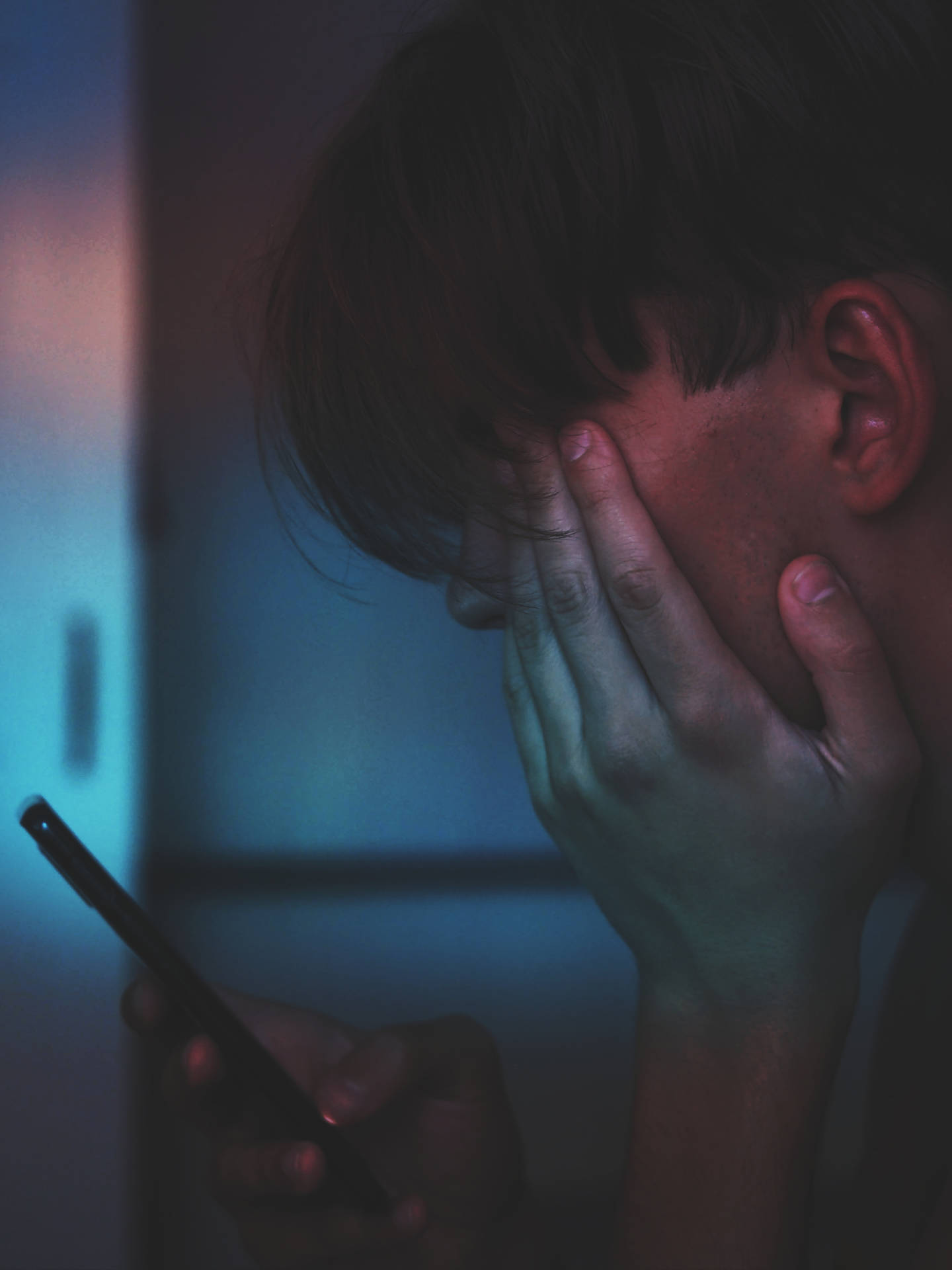 人在昏暗藍光下拿著電話並遮住臉