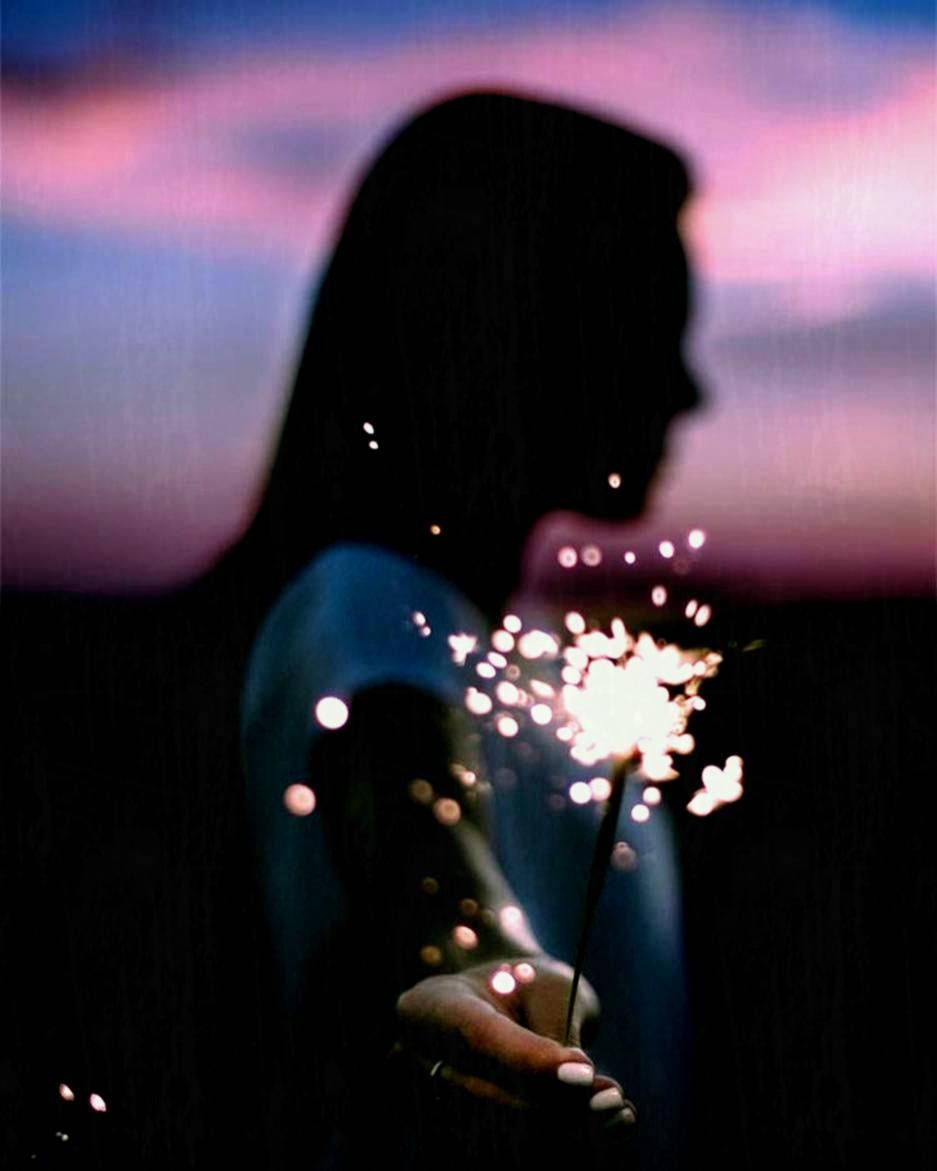 傷感少女手持煙火 壁紙 — 一個人的剪影，在帶有粉紅色和紫色色調的暮色天空中手持閃爍的煙火。